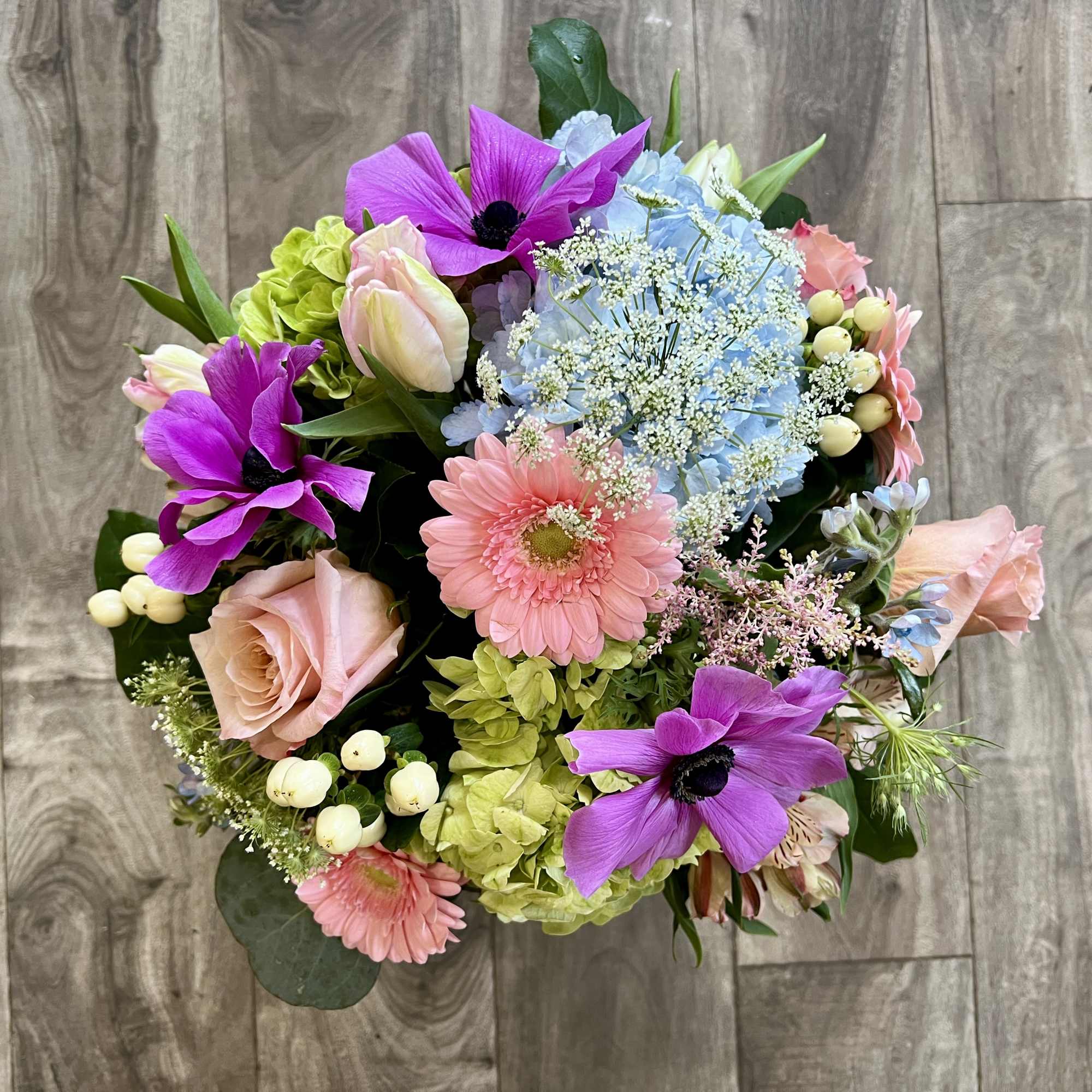 Mixed bouquet with pink roses, purple anemones, blue hydrangea, and a pink gerbera daisy