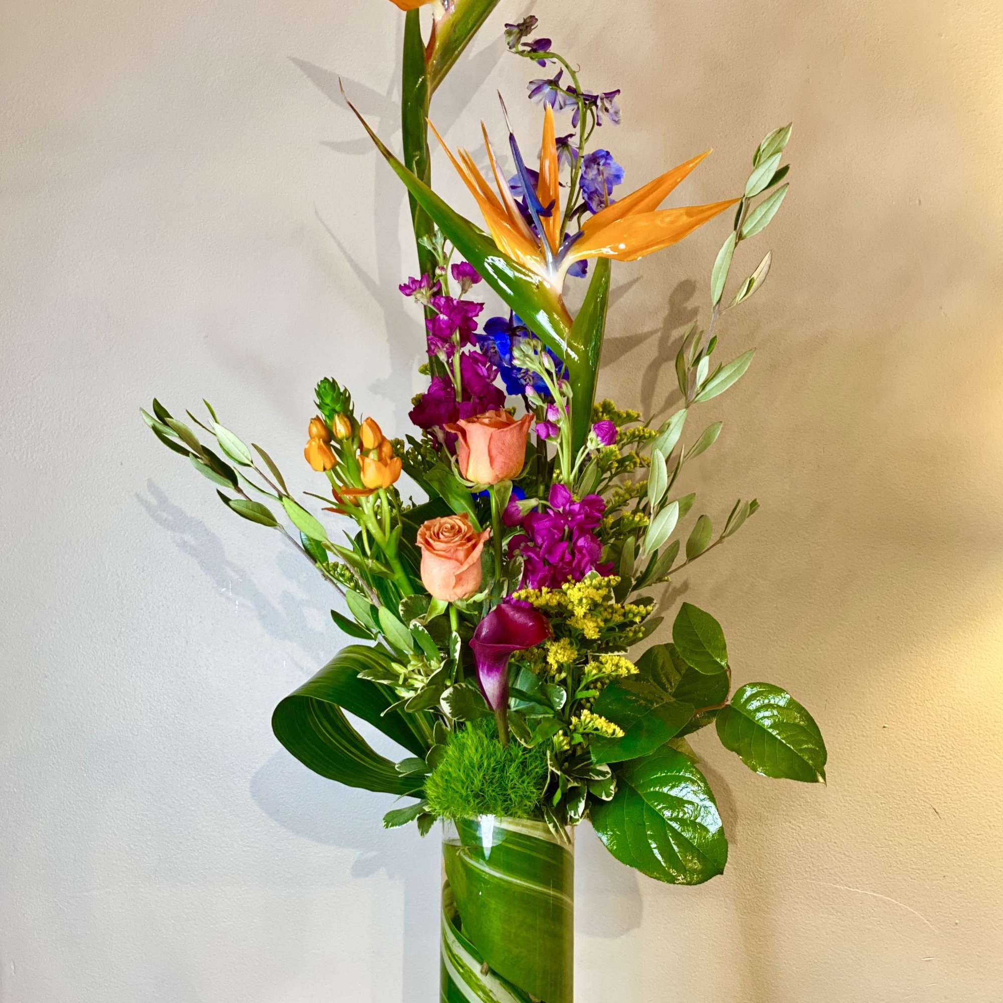 Tall tropical bouquet with orange bird of paradise and pink roses in a glass vase