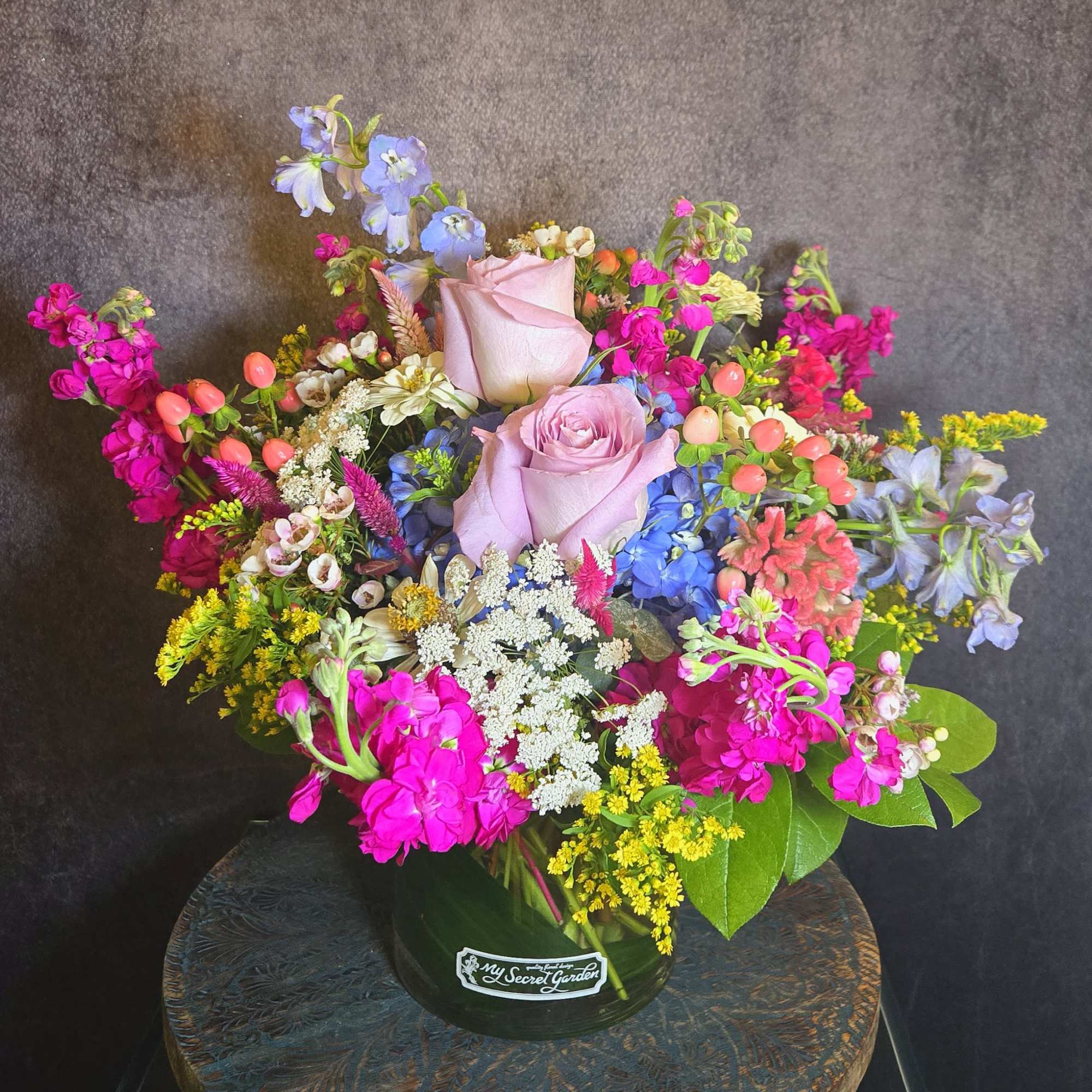 Mixed bouquet of pink roses, blue flowers, and bright magenta blooms in a vase