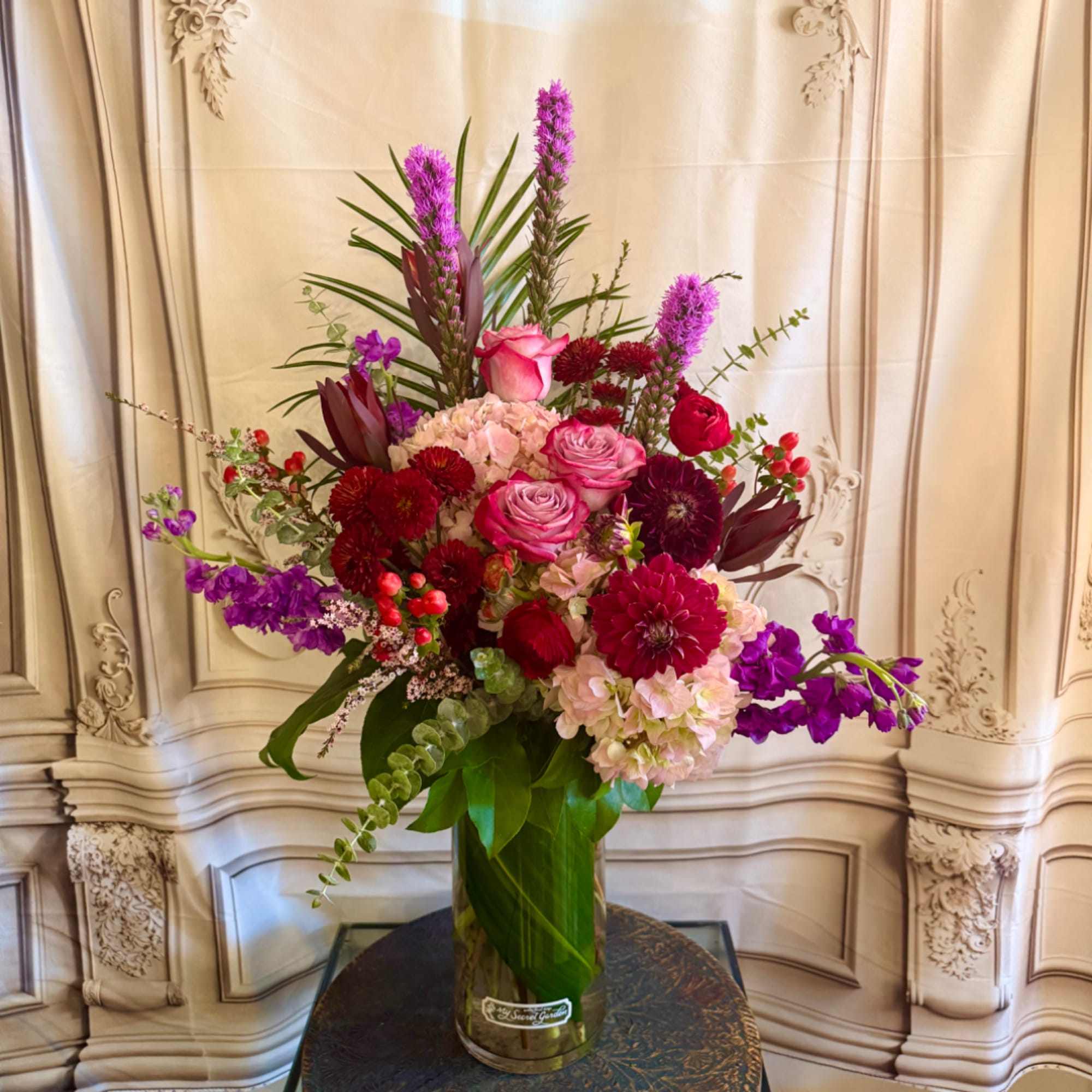 Tall mixed bouquet in a glass vase with pink, red, and purple flowers