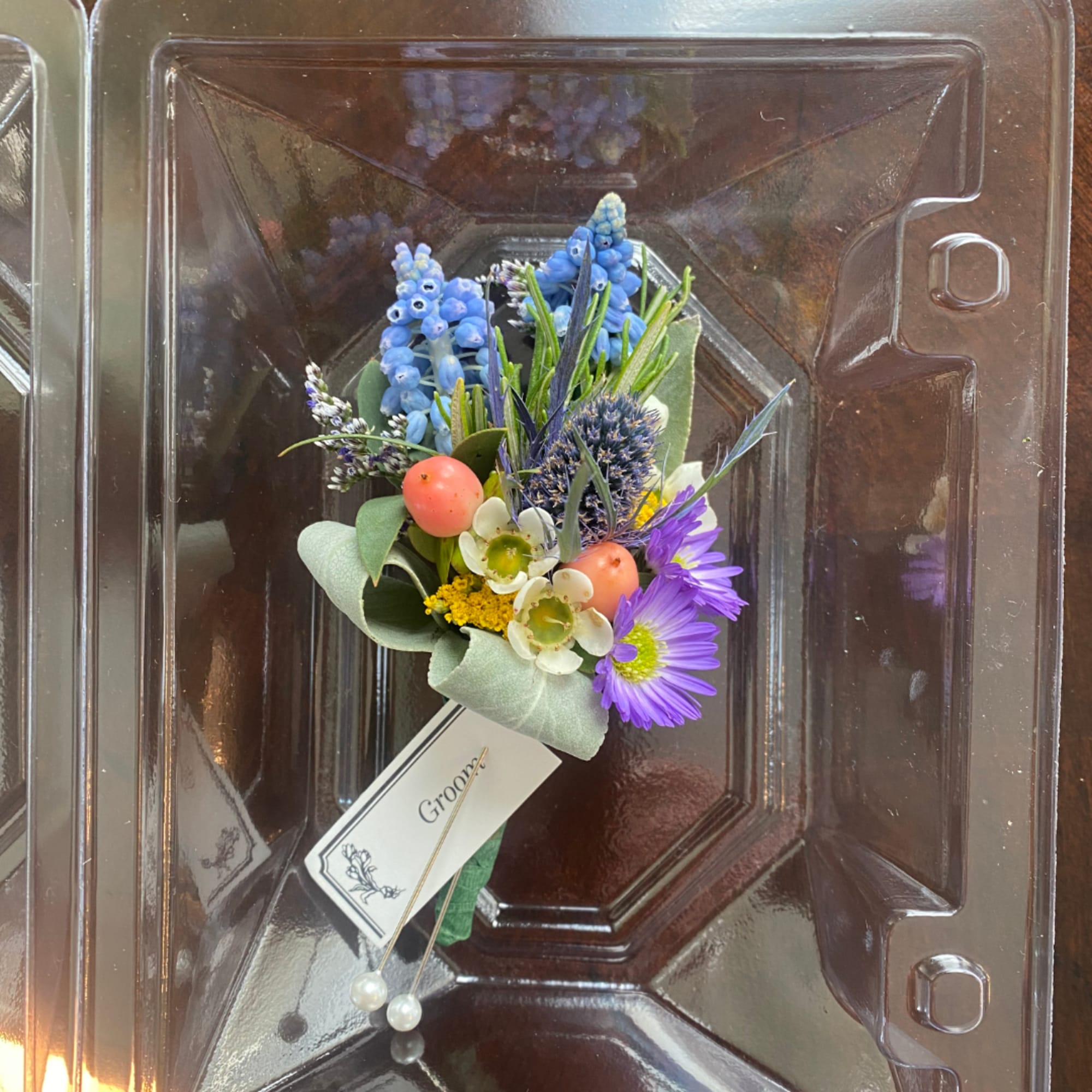 Small boutonniere with blue and purple flowers in a plastic box