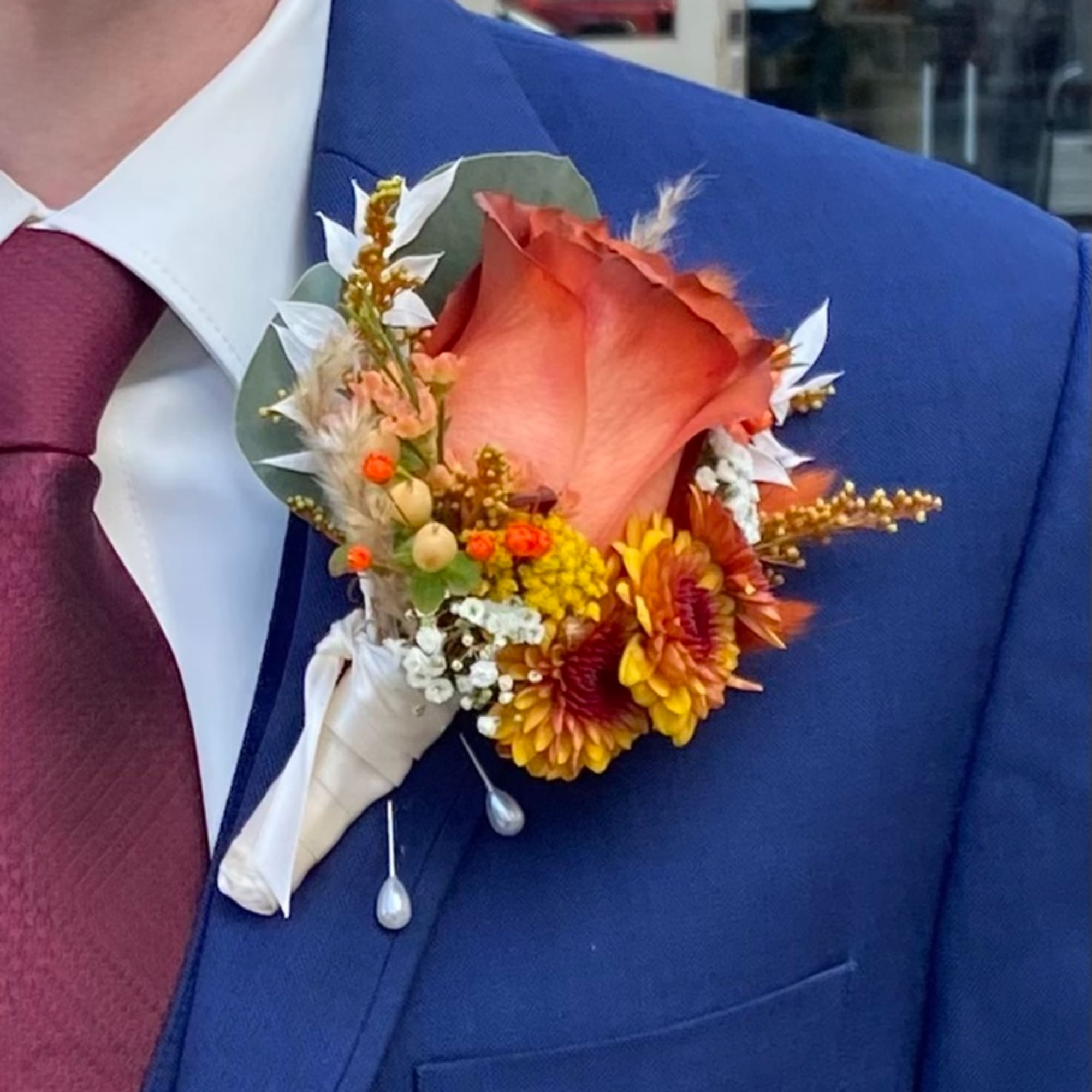 Boutonniere with an orange rose and small mixed flowers on a blue suit jacket
