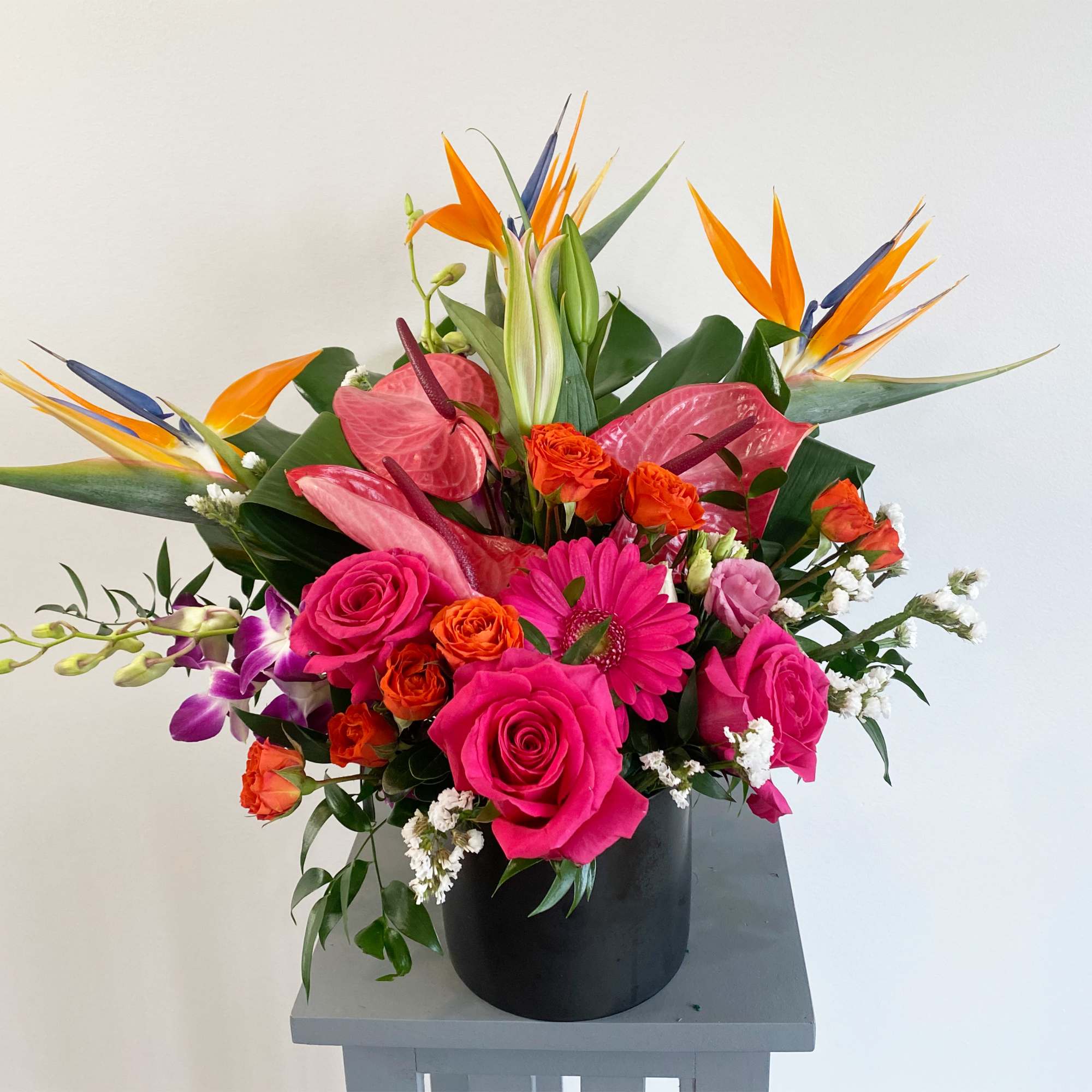 Bright tropical bouquet in a black vase with pink roses and orange bird-of-paradise
