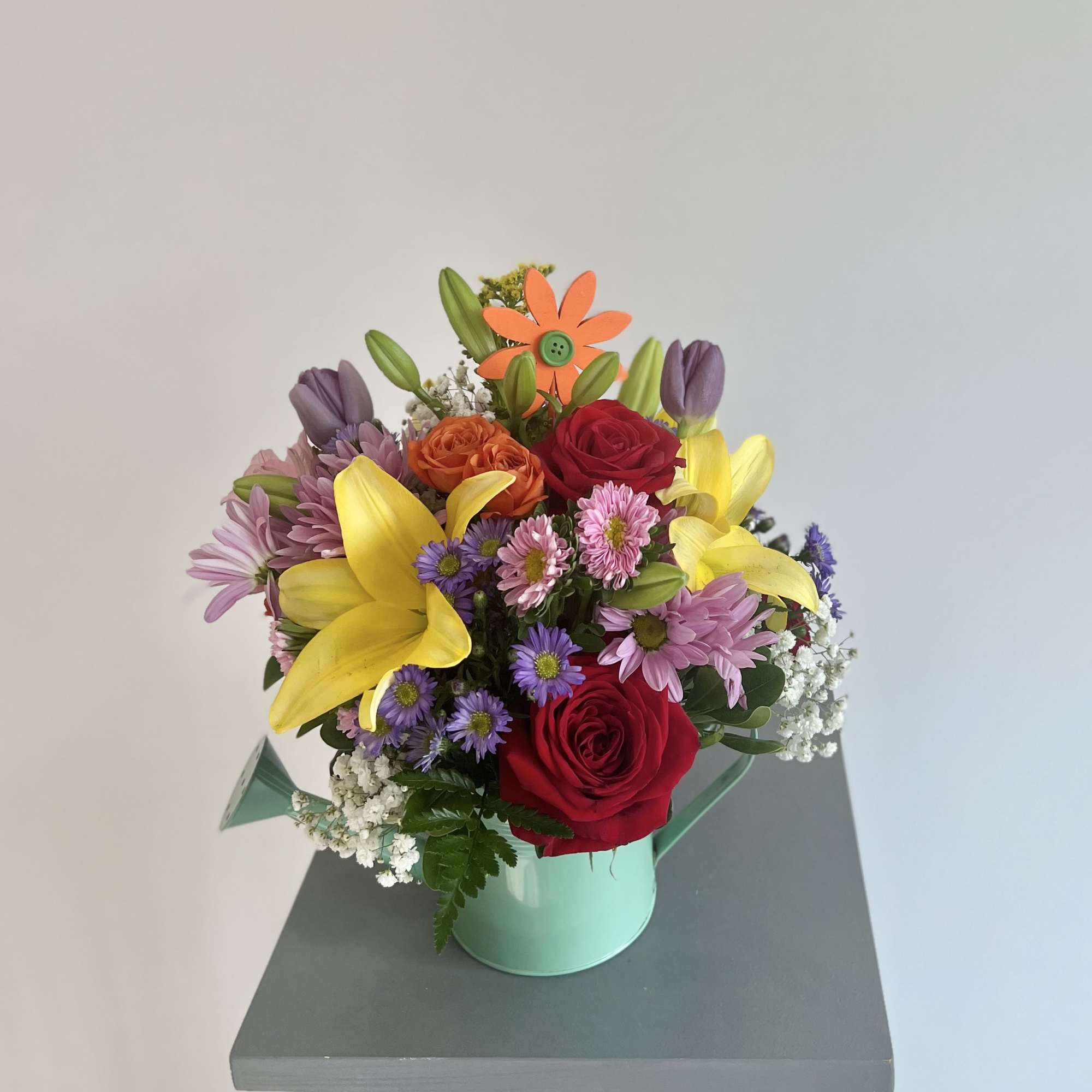 Mixed bouquet of roses, lilies, and daisies in a mint tin container