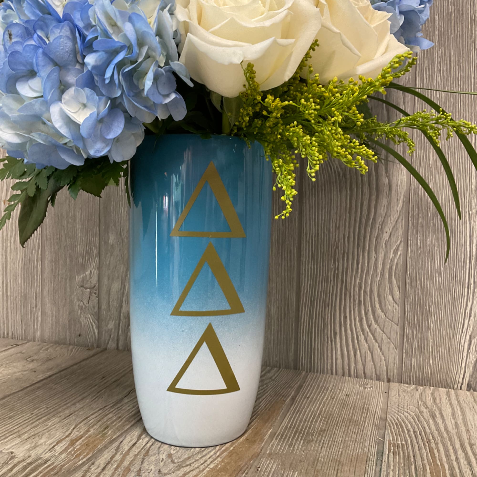 Blue and white floral arrangement in a tall gradient vase