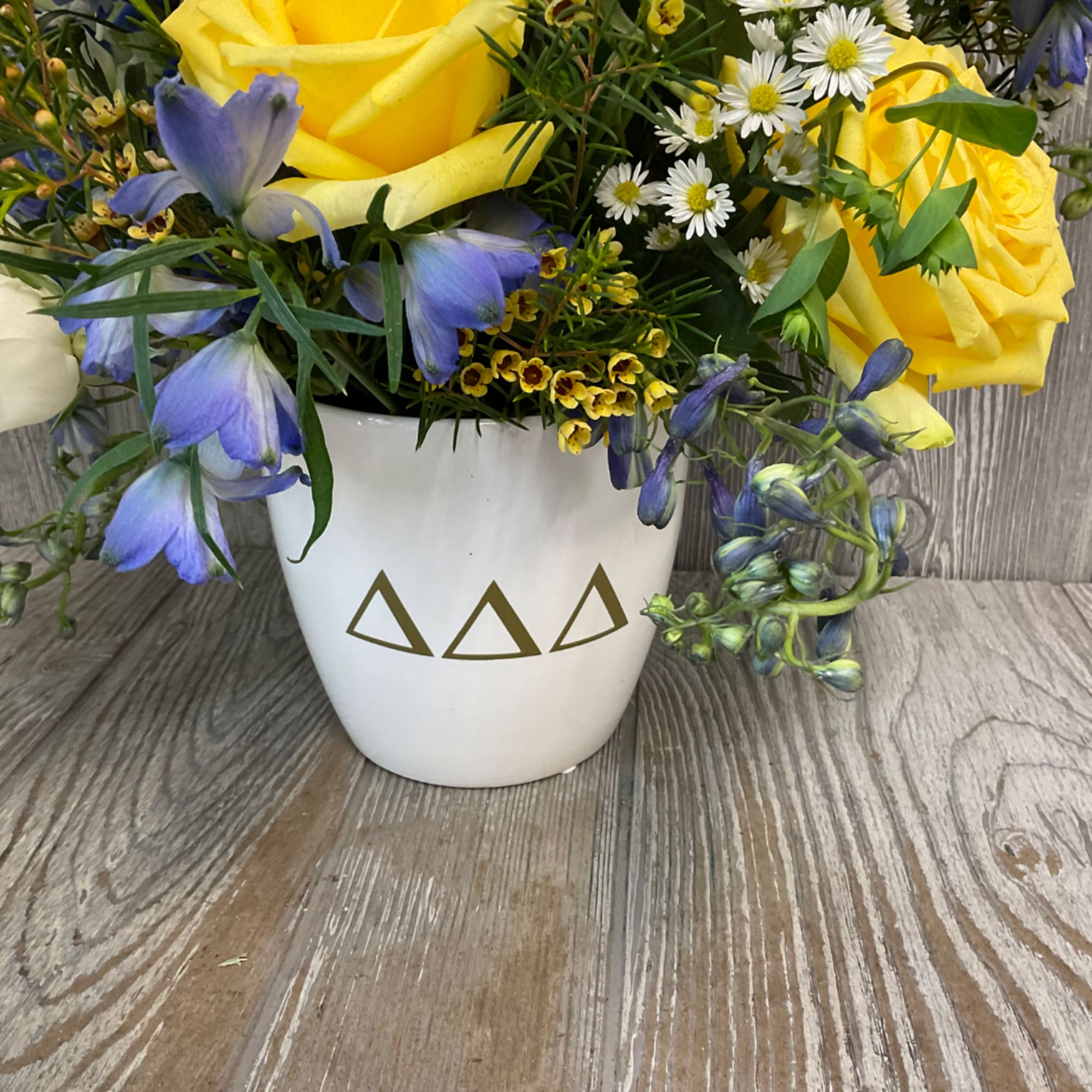 Yellow roses and blue flowers in a white vase