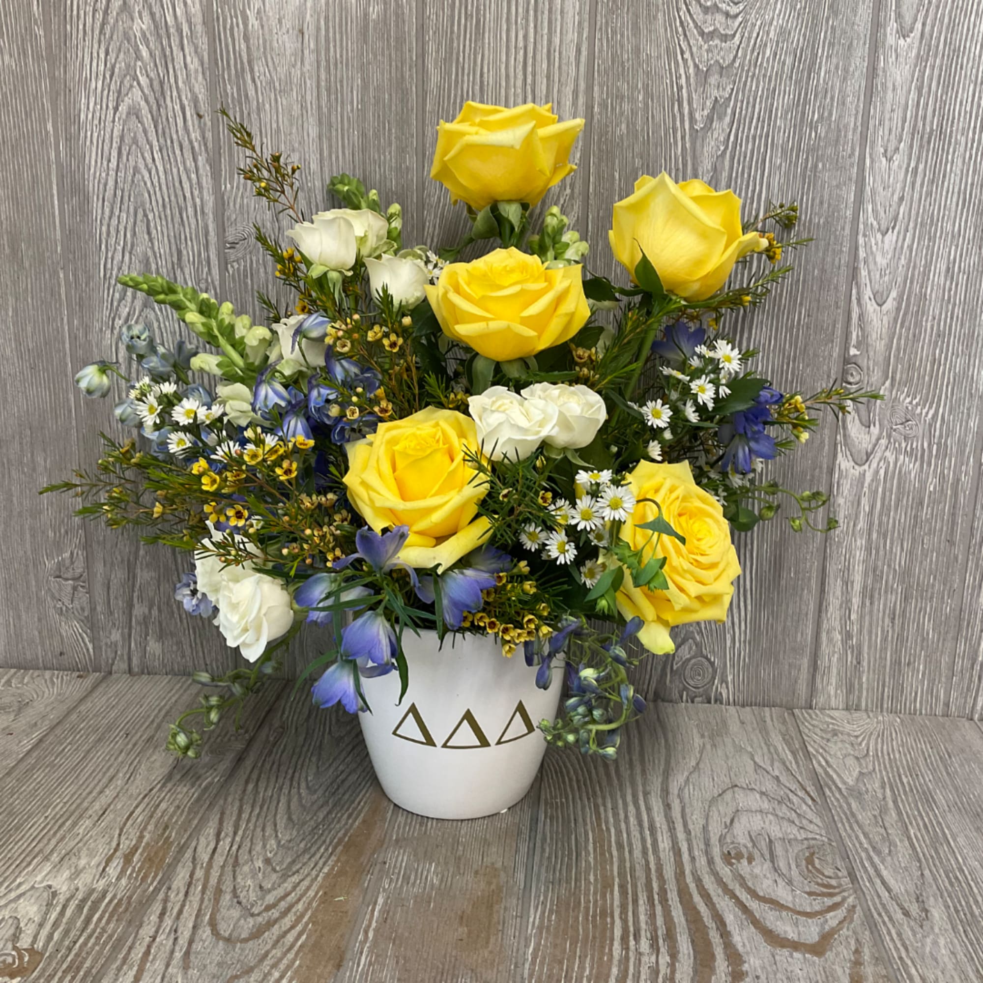 Yellow and white roses with blue flowers in a white vase
