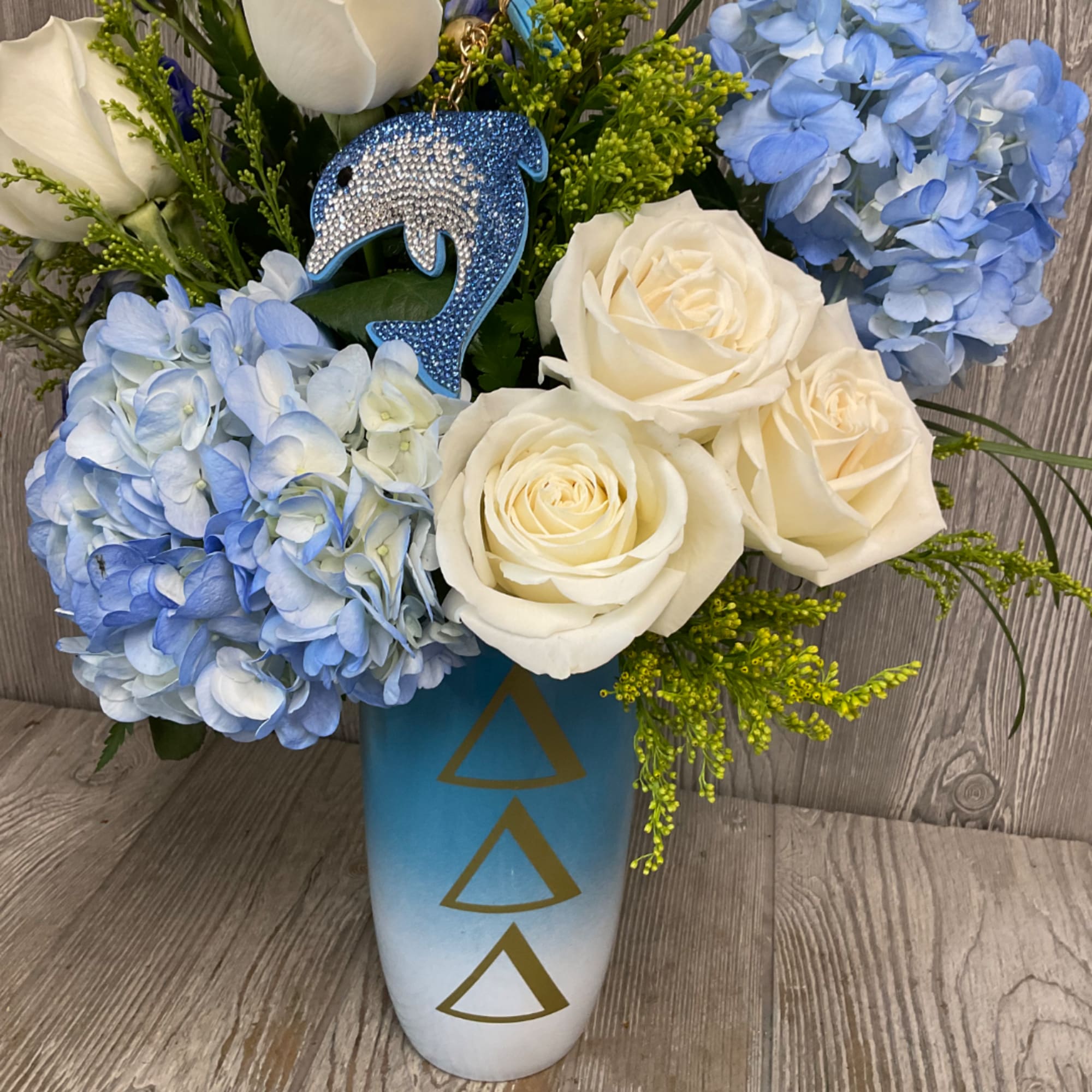 Blue hydrangeas and white roses in a tall blue vase with a dolphin ornament.