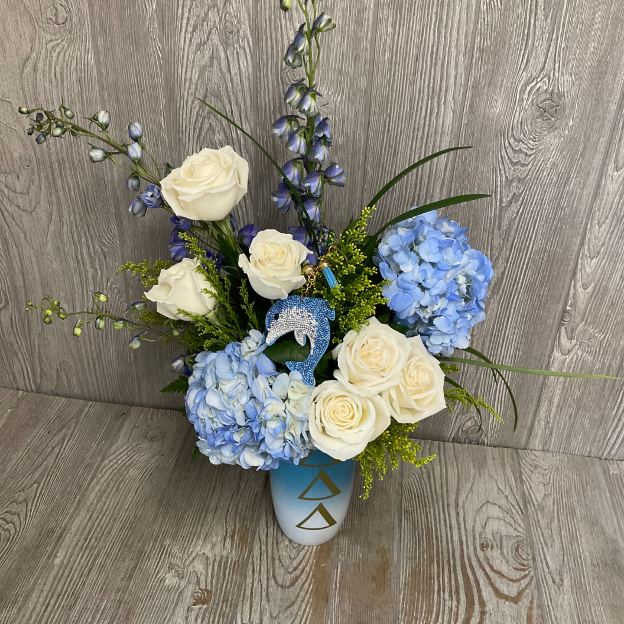 Blue hydrangeas and white roses arranged in a blue vase with a dolphin ornament.