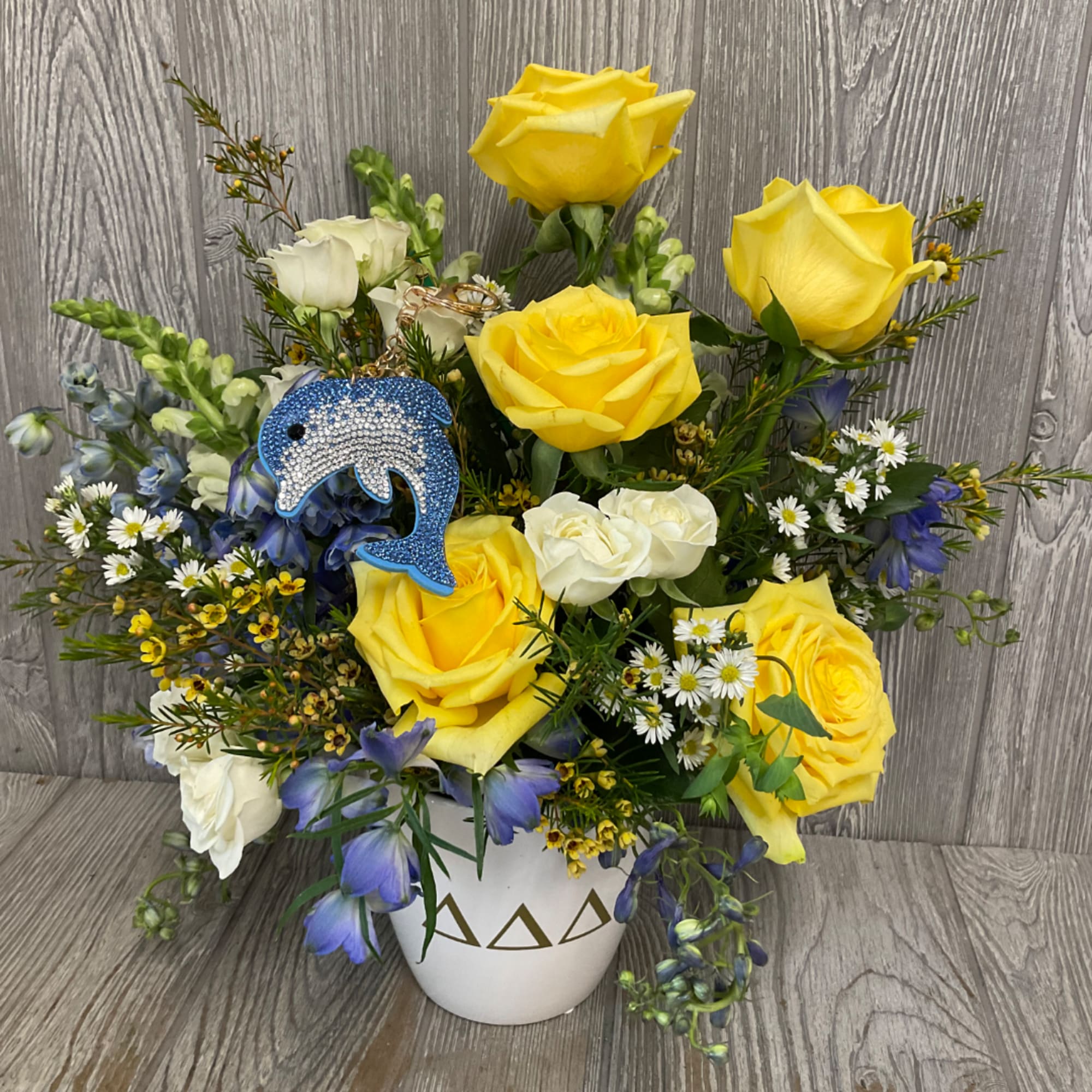 Yellow and white roses in a white vase with a blue dolphin ornament