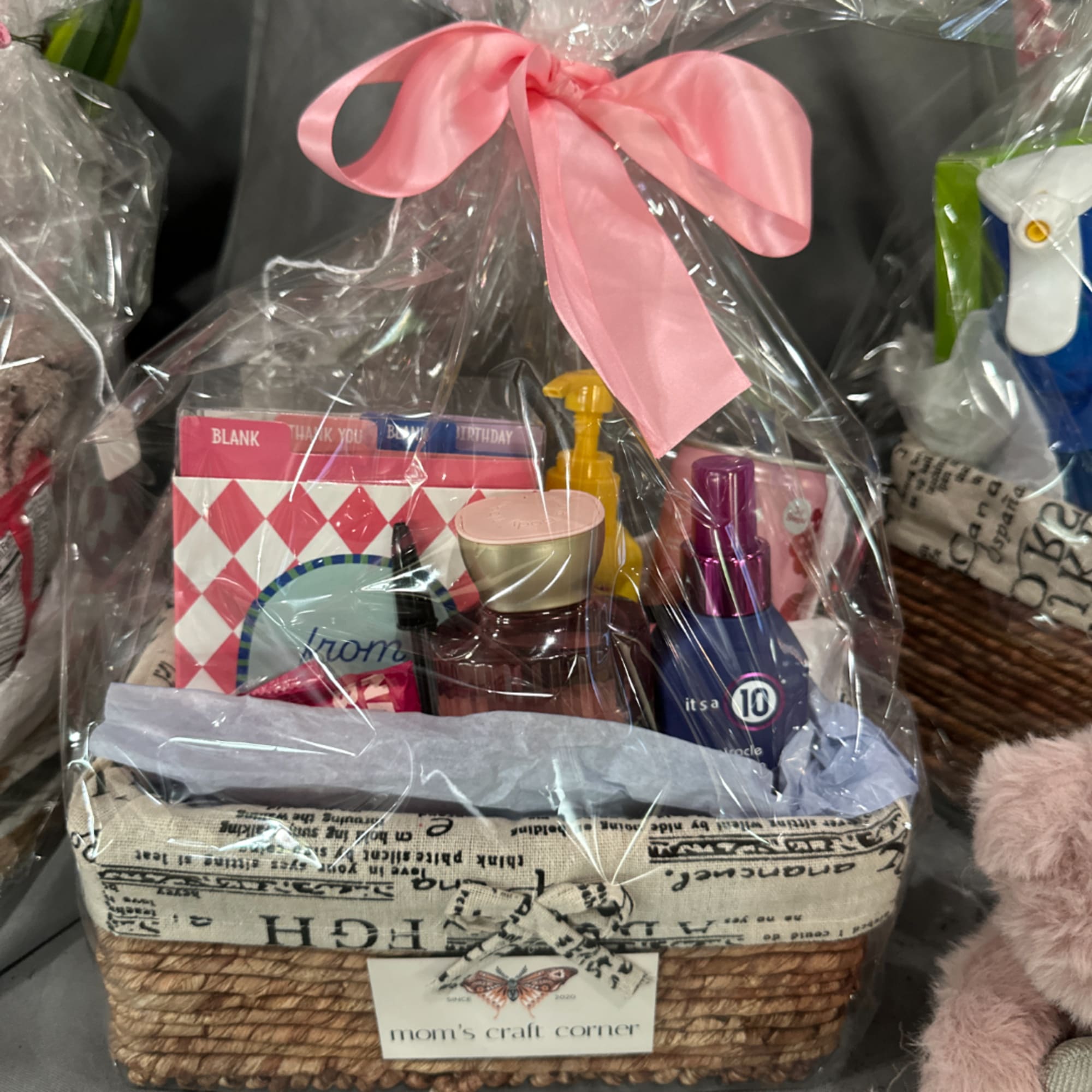 Gift basket with toiletries and greeting cards wrapped in clear plastic and a pink bow