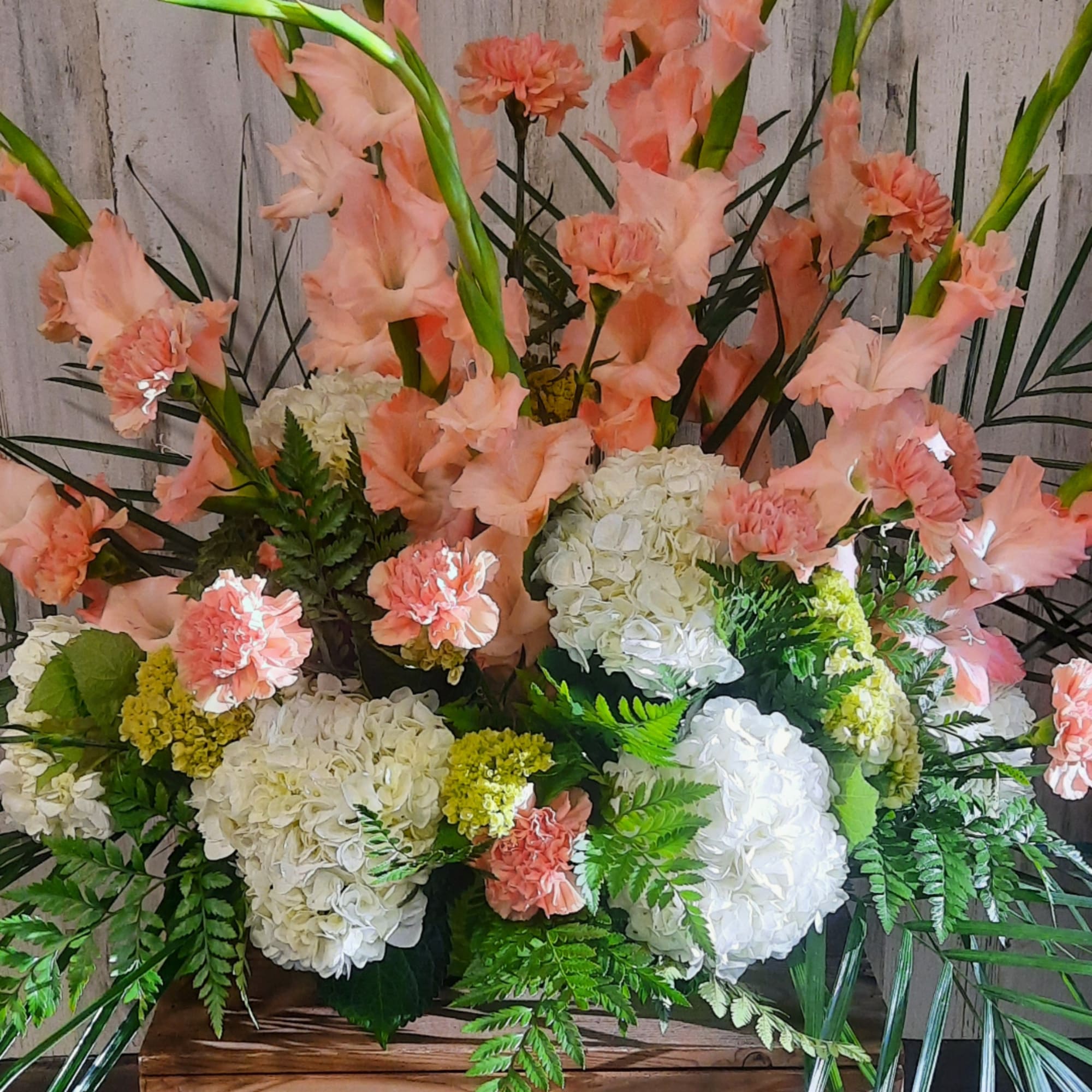 Arrangement of peach gladiolus, white hydrangeas, and carnations in a wooden container