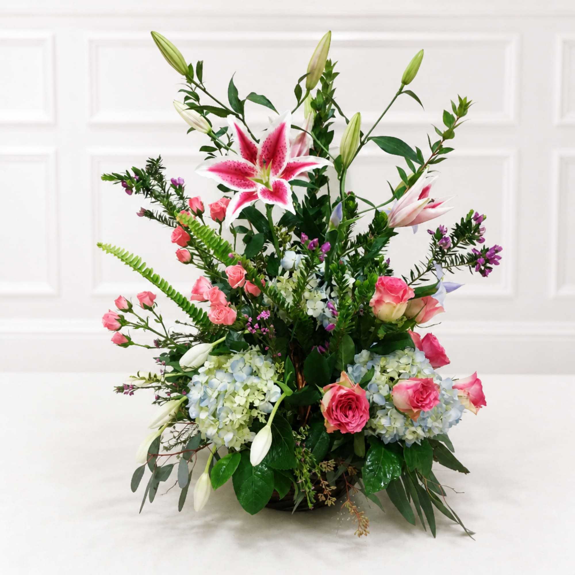 Tall floral arrangement with pink lilies, roses, hydrangeas, and buds in a low container