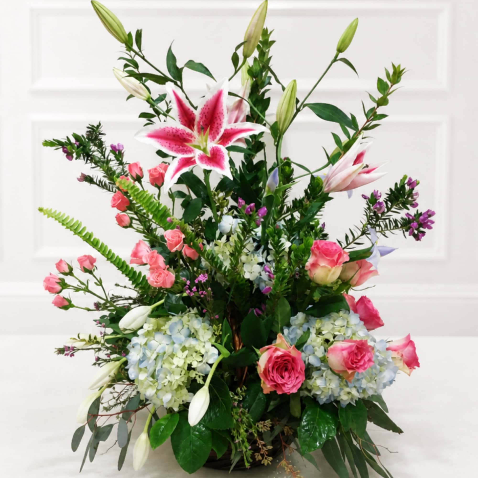 Tall floral arrangement with pink lilies, pink roses, and blue hydrangeas in a vase