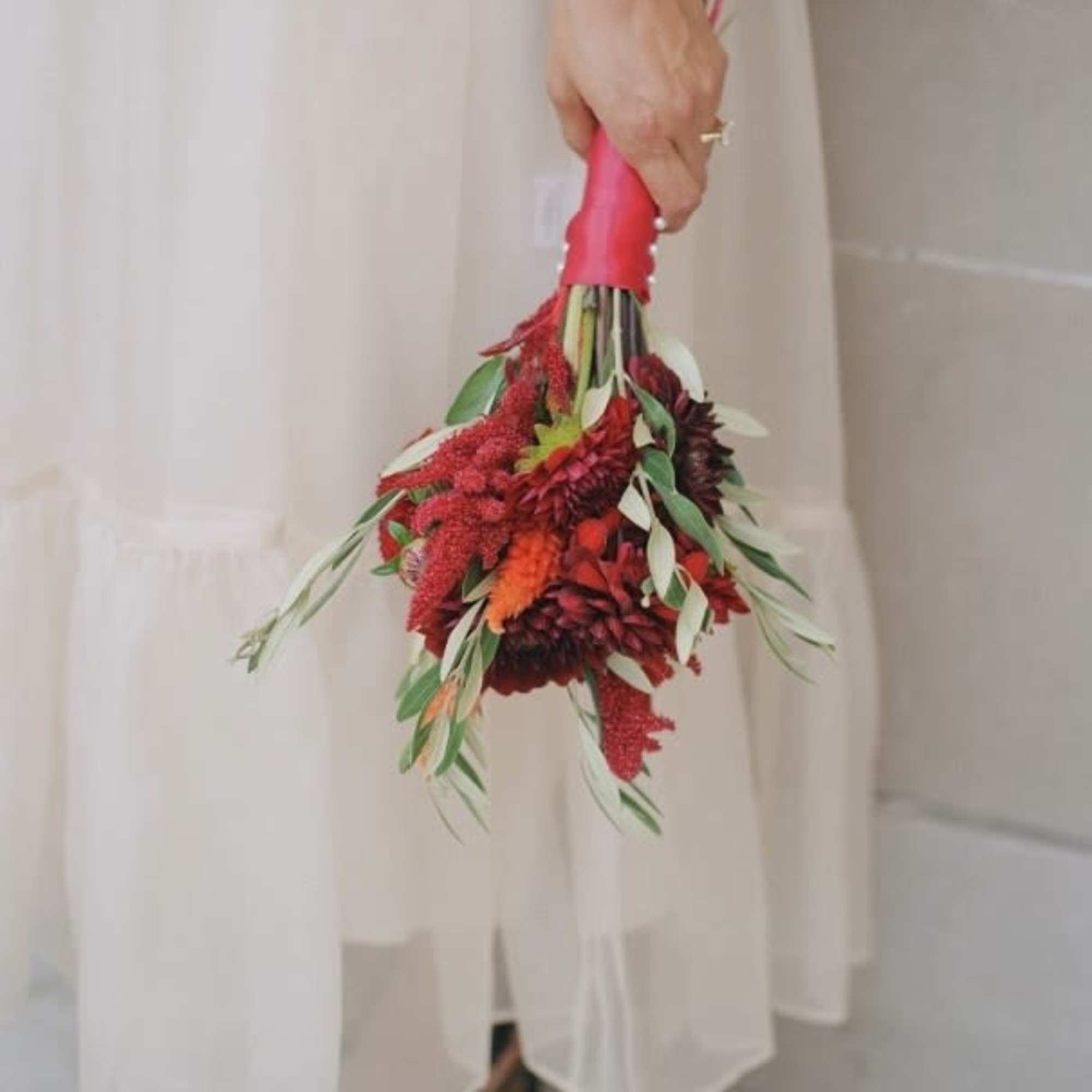 Handheld bouquet of red flowers with green foliage and a pink wrap
