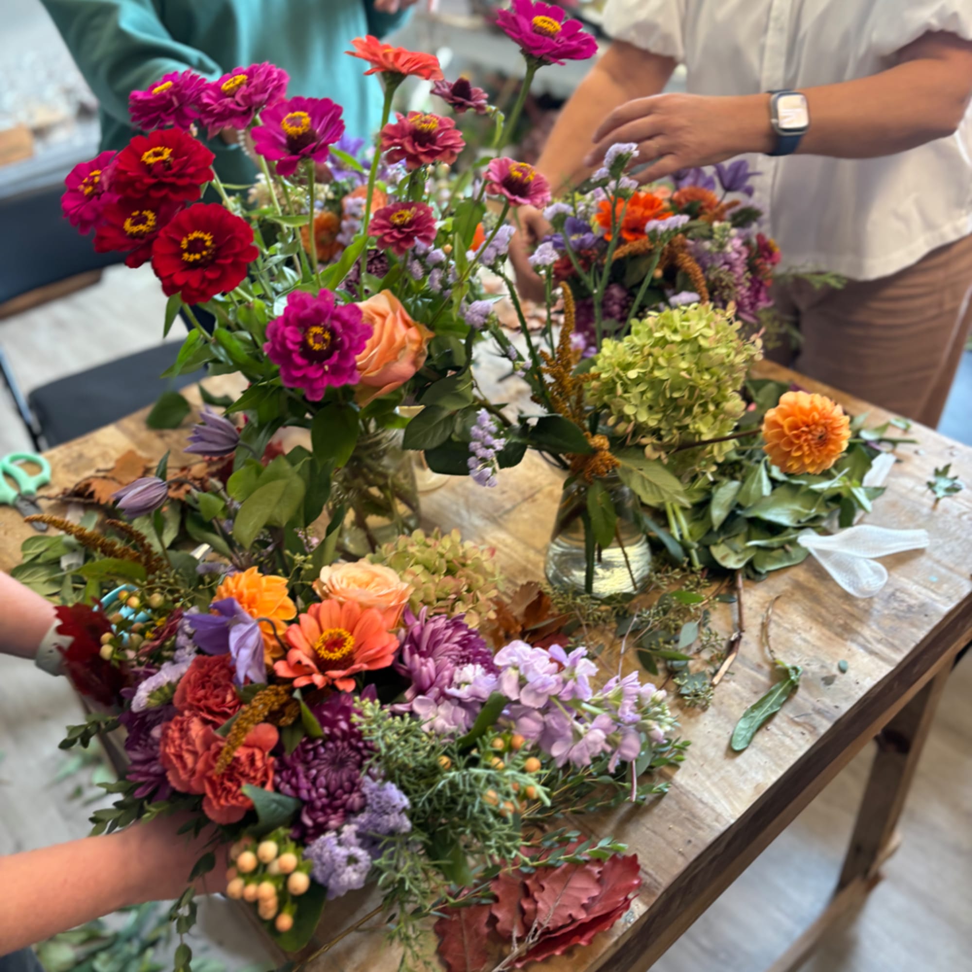 Colorful mixed bouquets on a wooden table with people arranging them