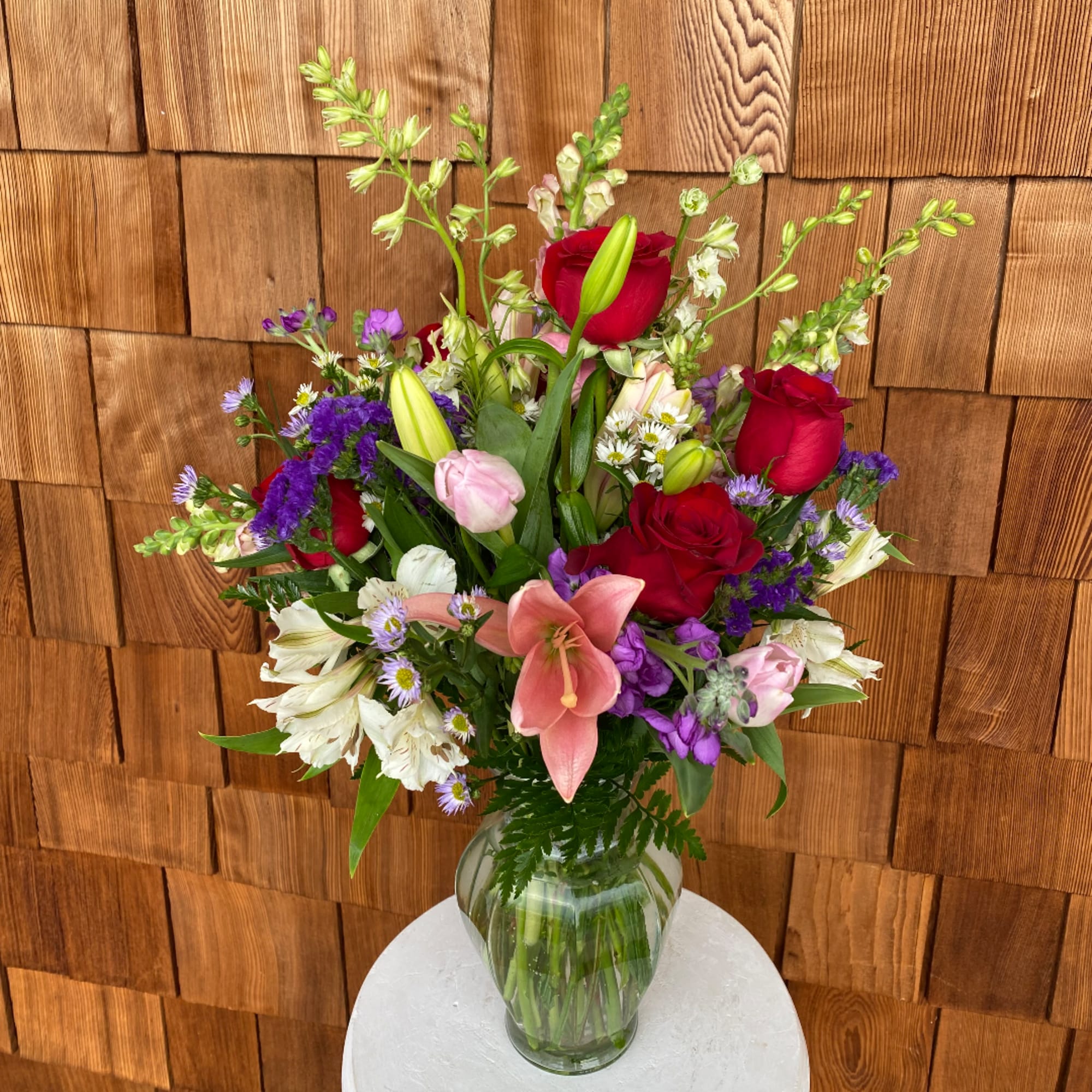 Mixed bouquet of red roses, pink lilies, and purple flowers in a glass vase
