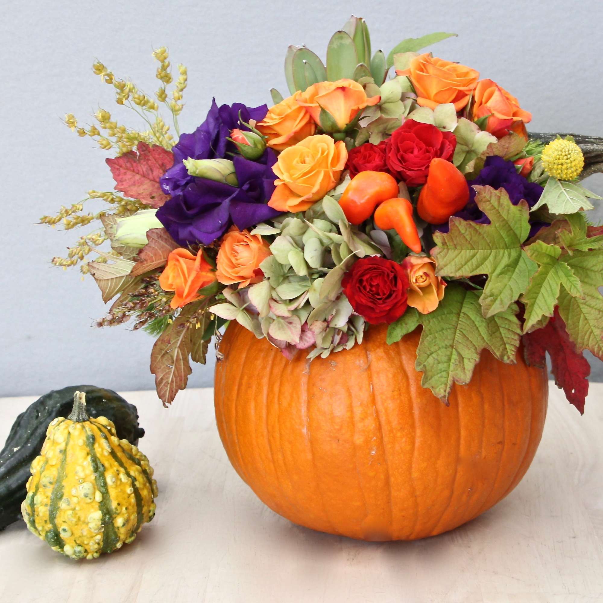 Autumn flower arrangement with roses and lisianthus in a hollow pumpkin with decorative gourds