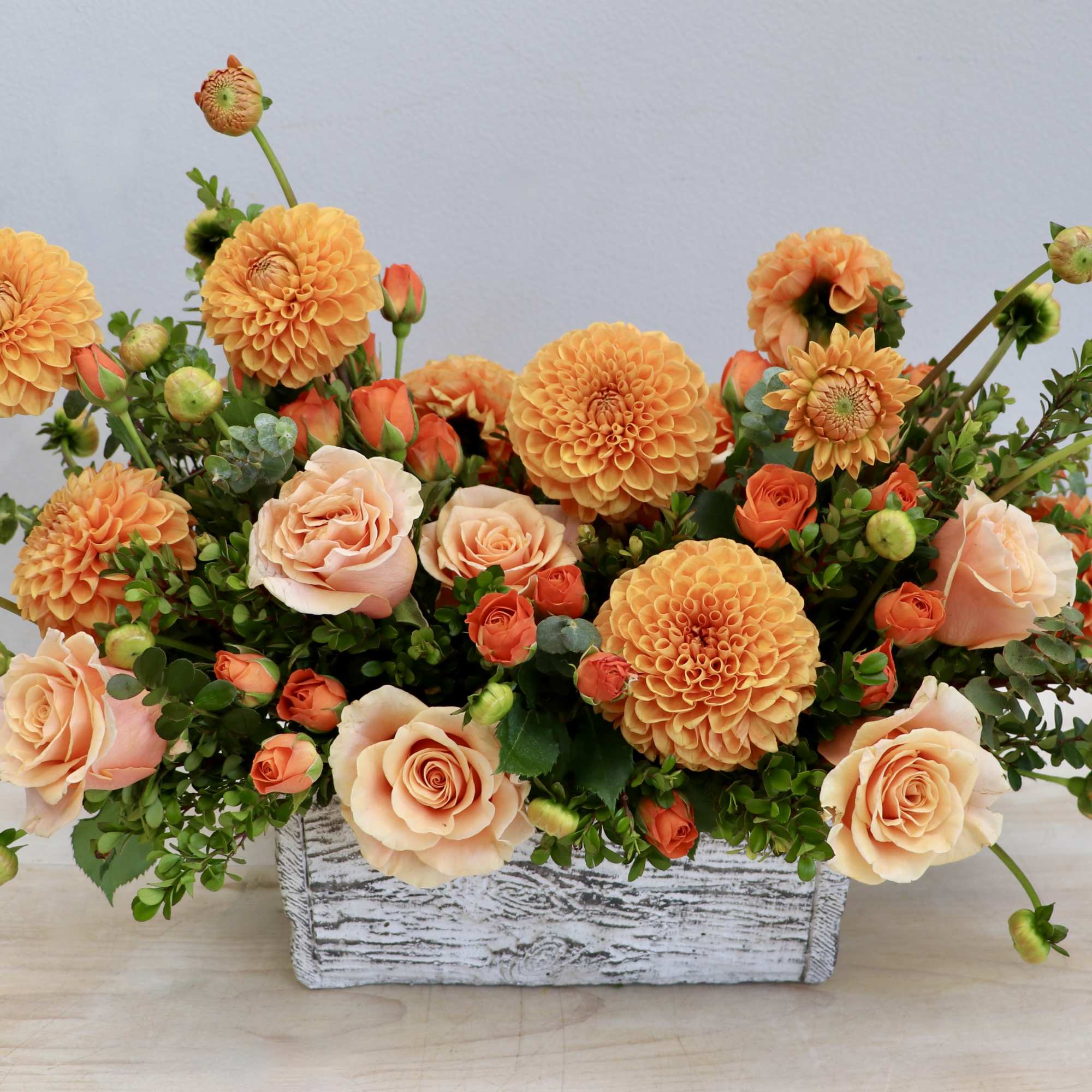 Low arrangement of orange dahlias and peach roses in a whitewashed wooden box