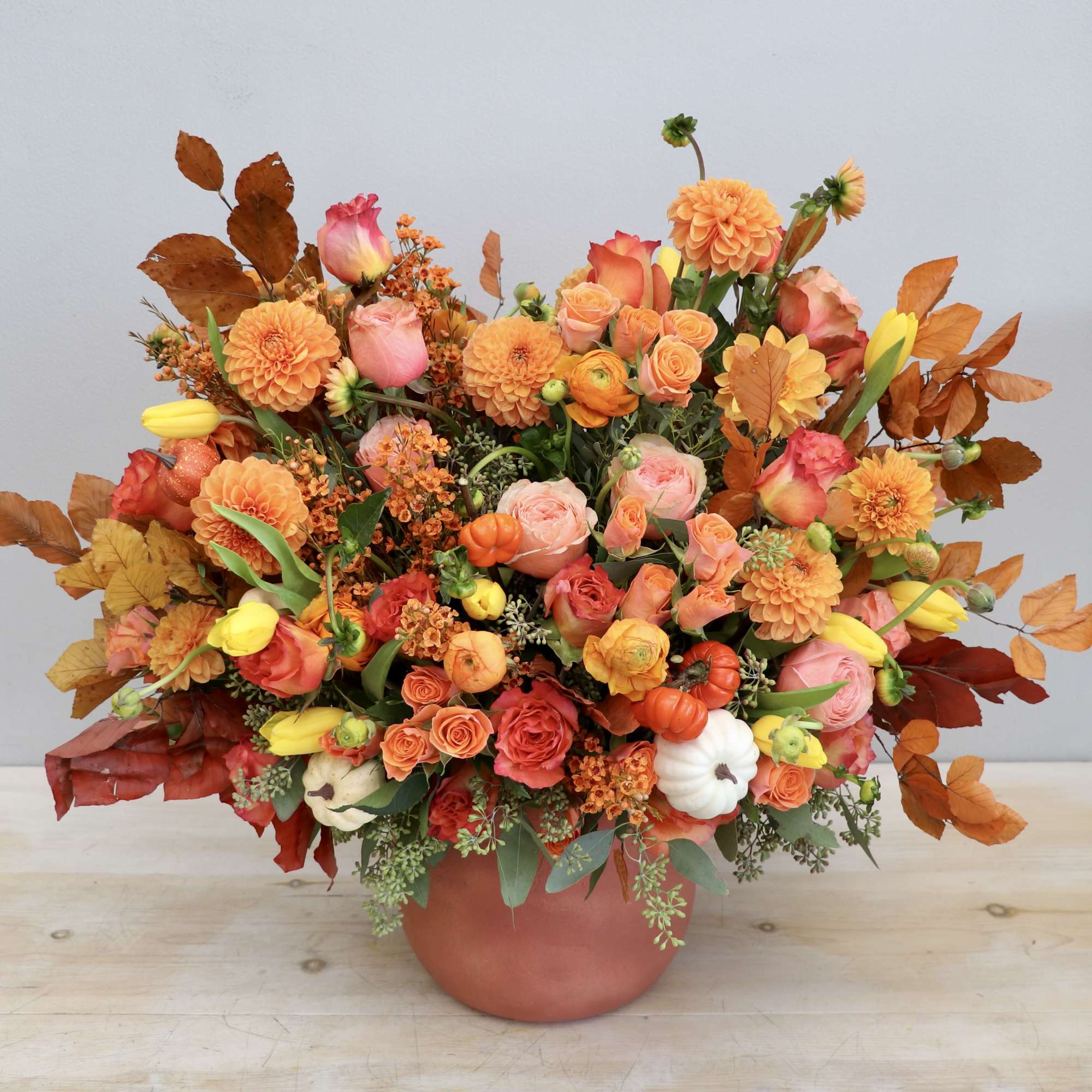 Large autumnal arrangement of orange dahlias, roses, and yellow tulips in a terracotta pot