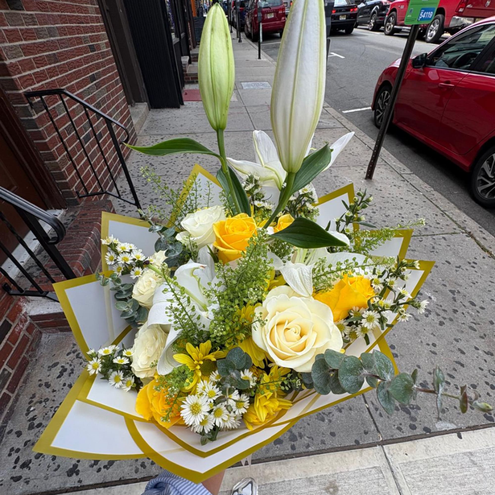 Bouquet of white lilies, yellow and white roses, and small daisies wrapped in white and gold paper