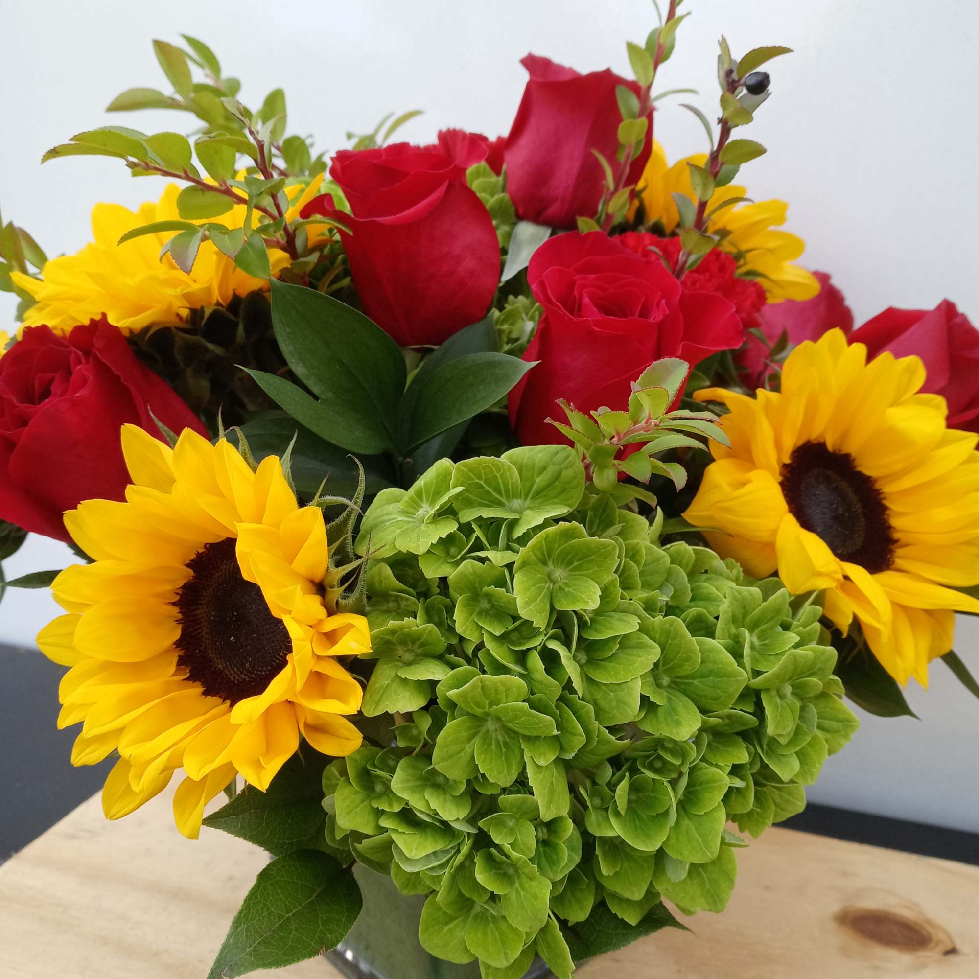 Bouquet of red roses, yellow sunflowers, and green hydrangea in a square vase