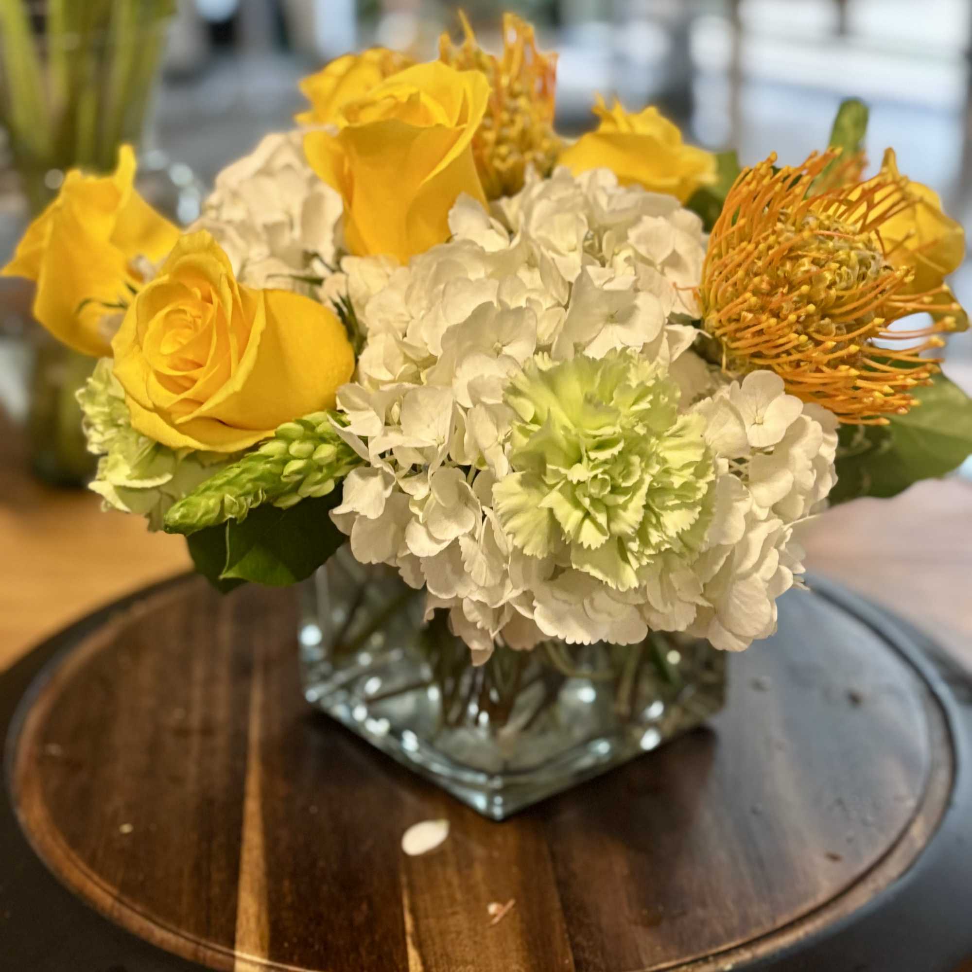 Yellow roses and white hydrangeas in a square glass vase