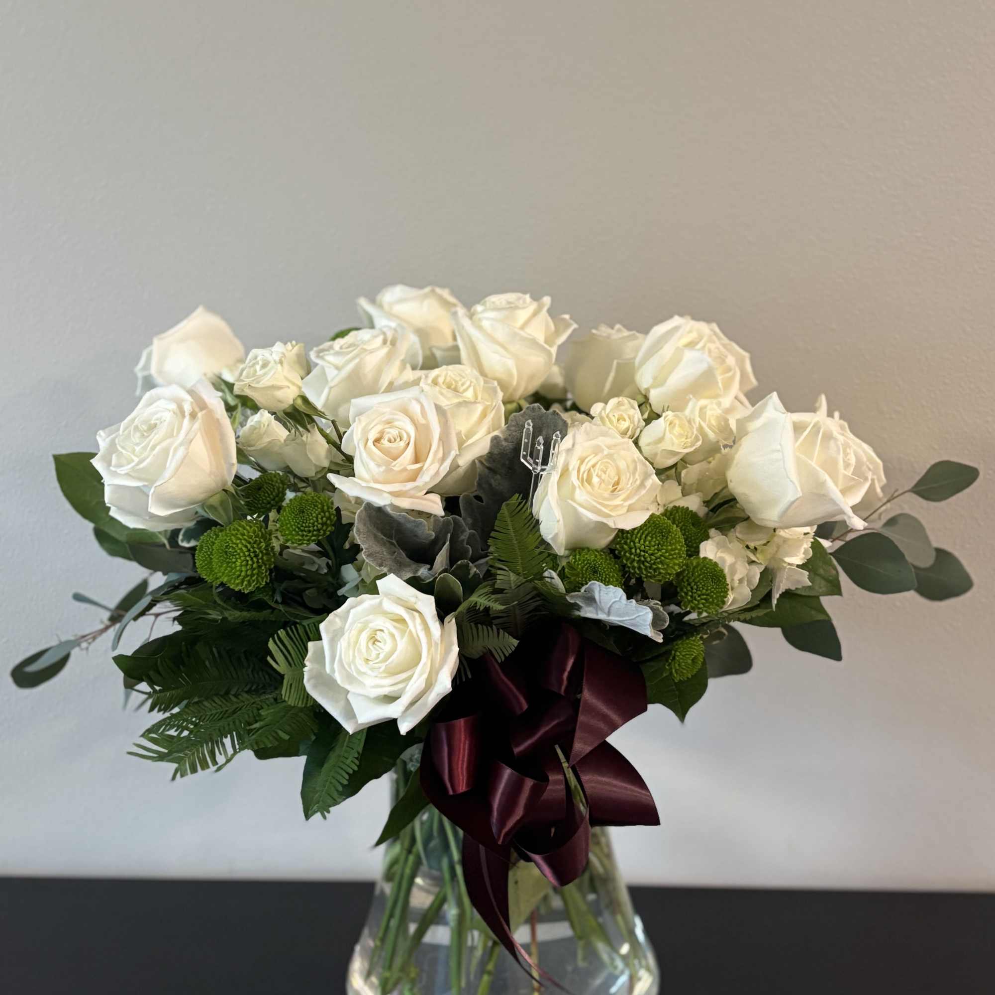 White rose bouquet in a clear glass vase with a burgundy ribbon