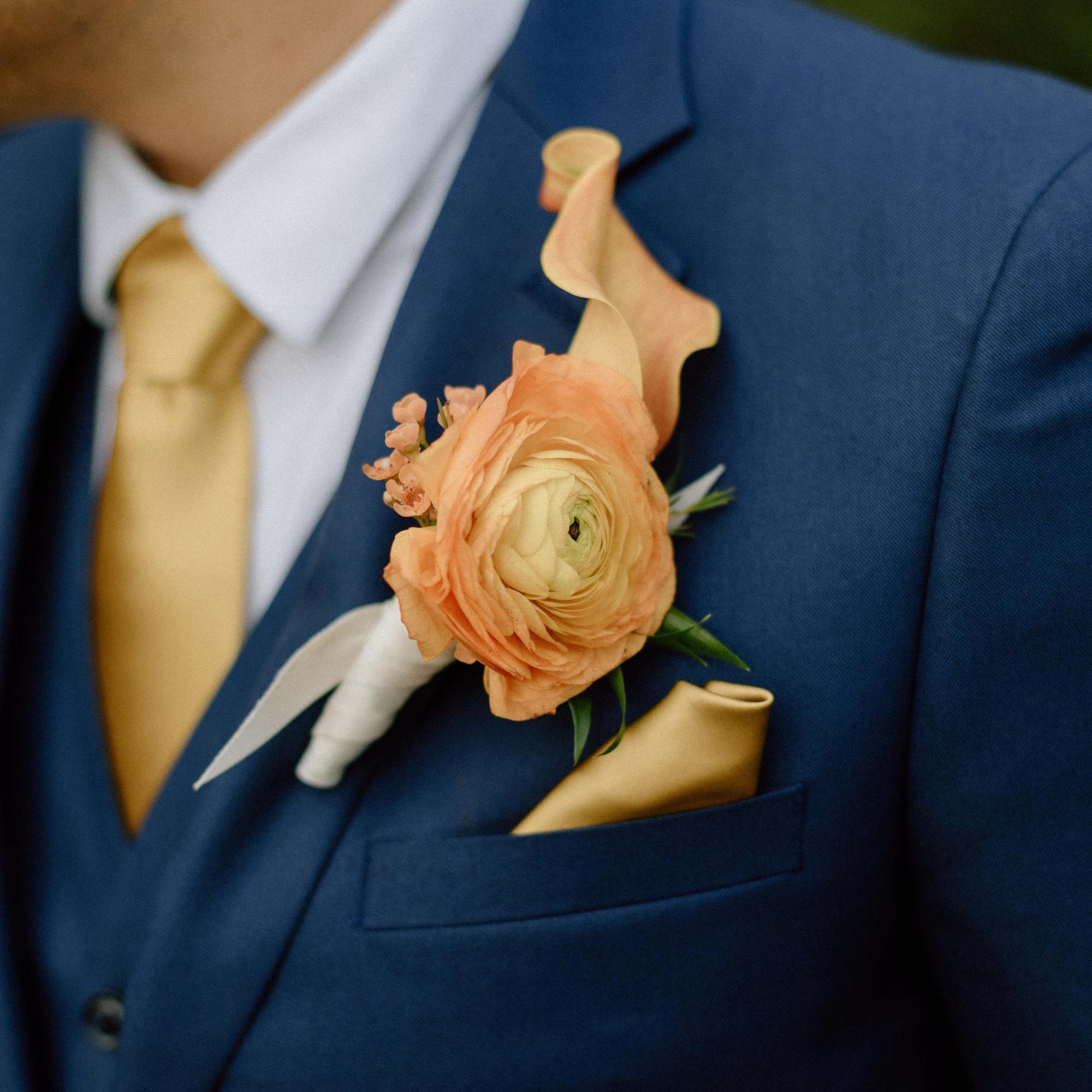 Peach boutonniere with a ranunculus flower on a blue suit jacket