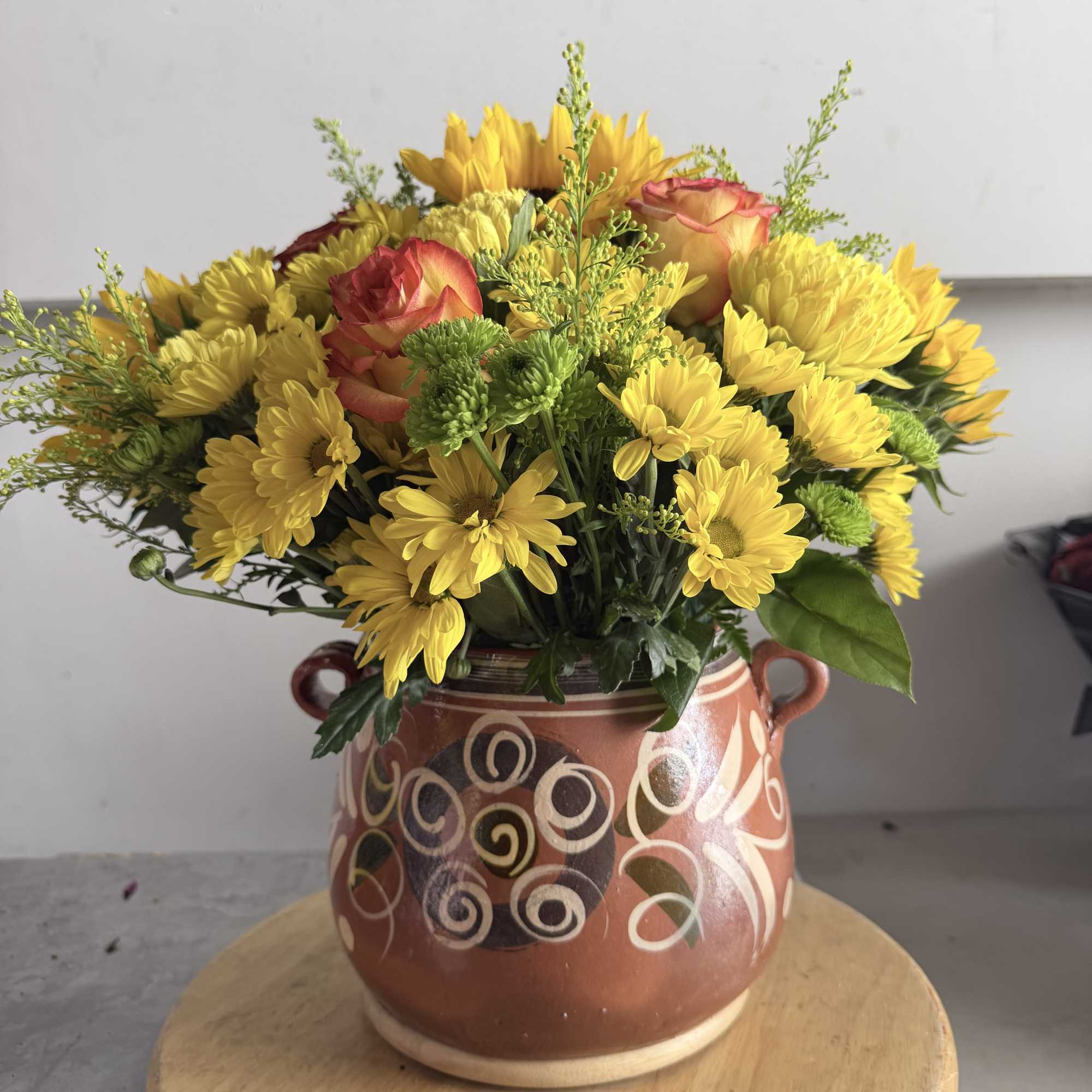 Yellow daisy bouquet with a few peach roses in a patterned ceramic vase