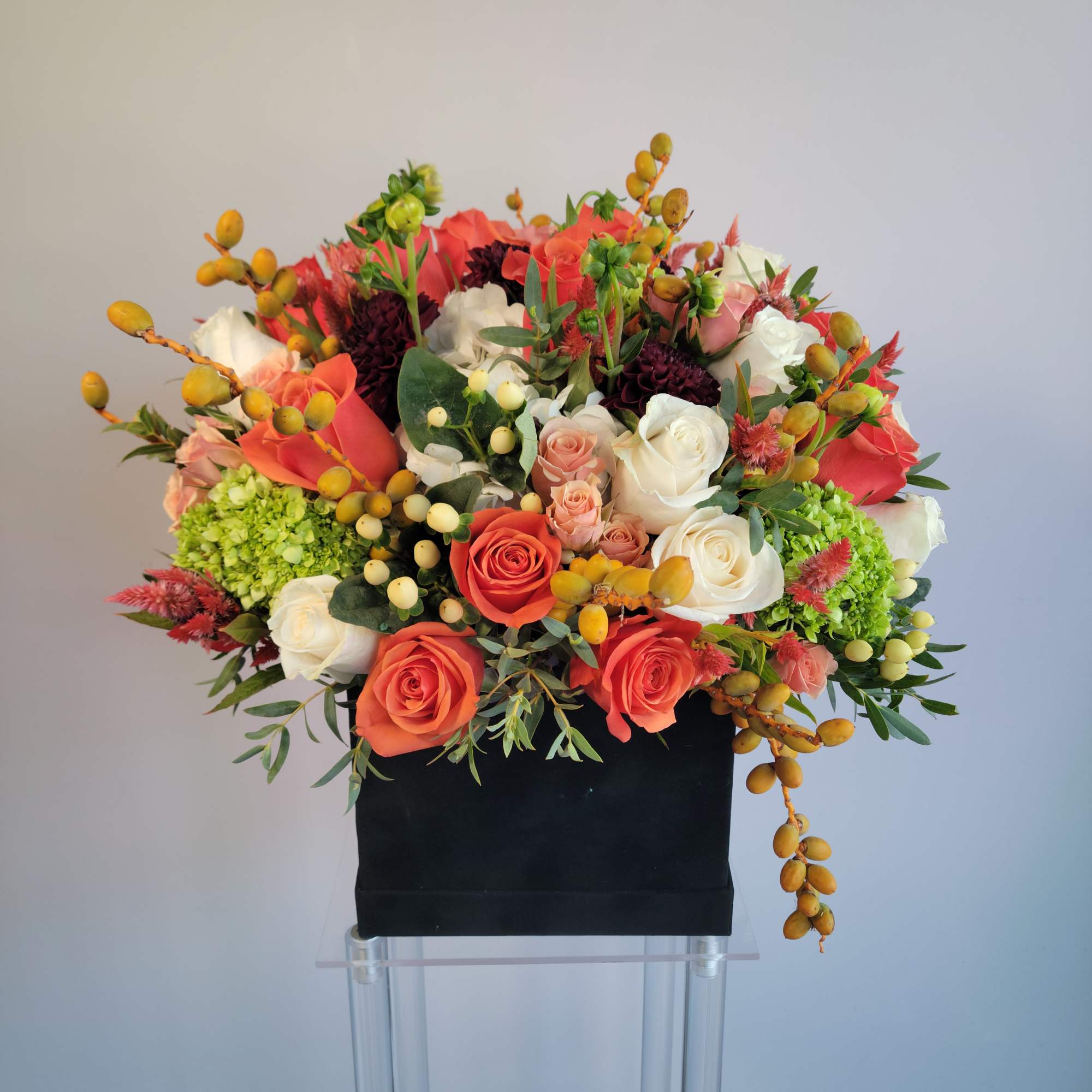 Compact arrangement of orange, peach, and white roses with green accents in a black box container