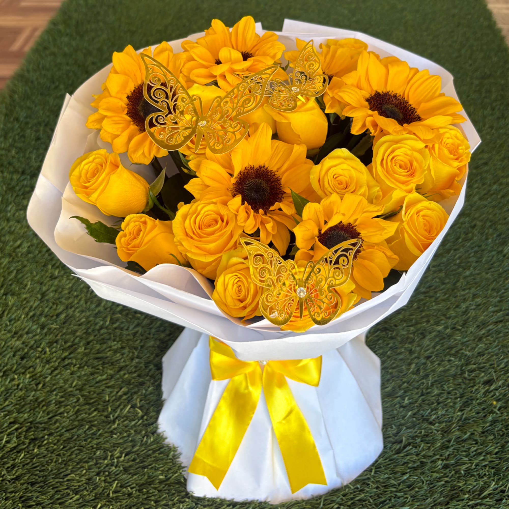 Yellow sunflower and rose bouquet wrapped in white paper with a yellow ribbon