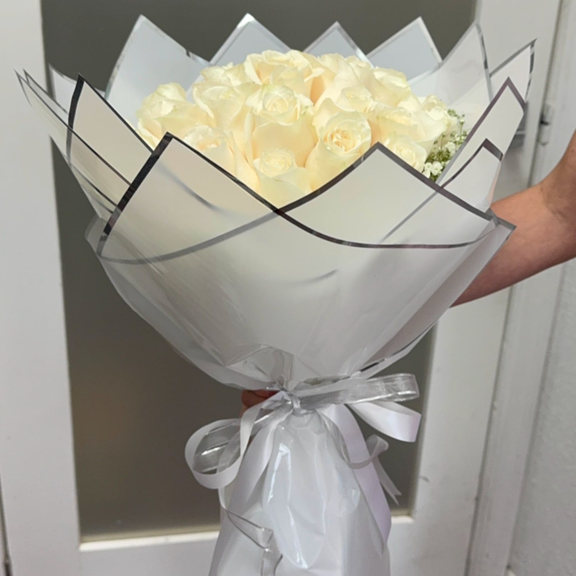 Bouquet of pale cream roses wrapped in white paper with a ribbon