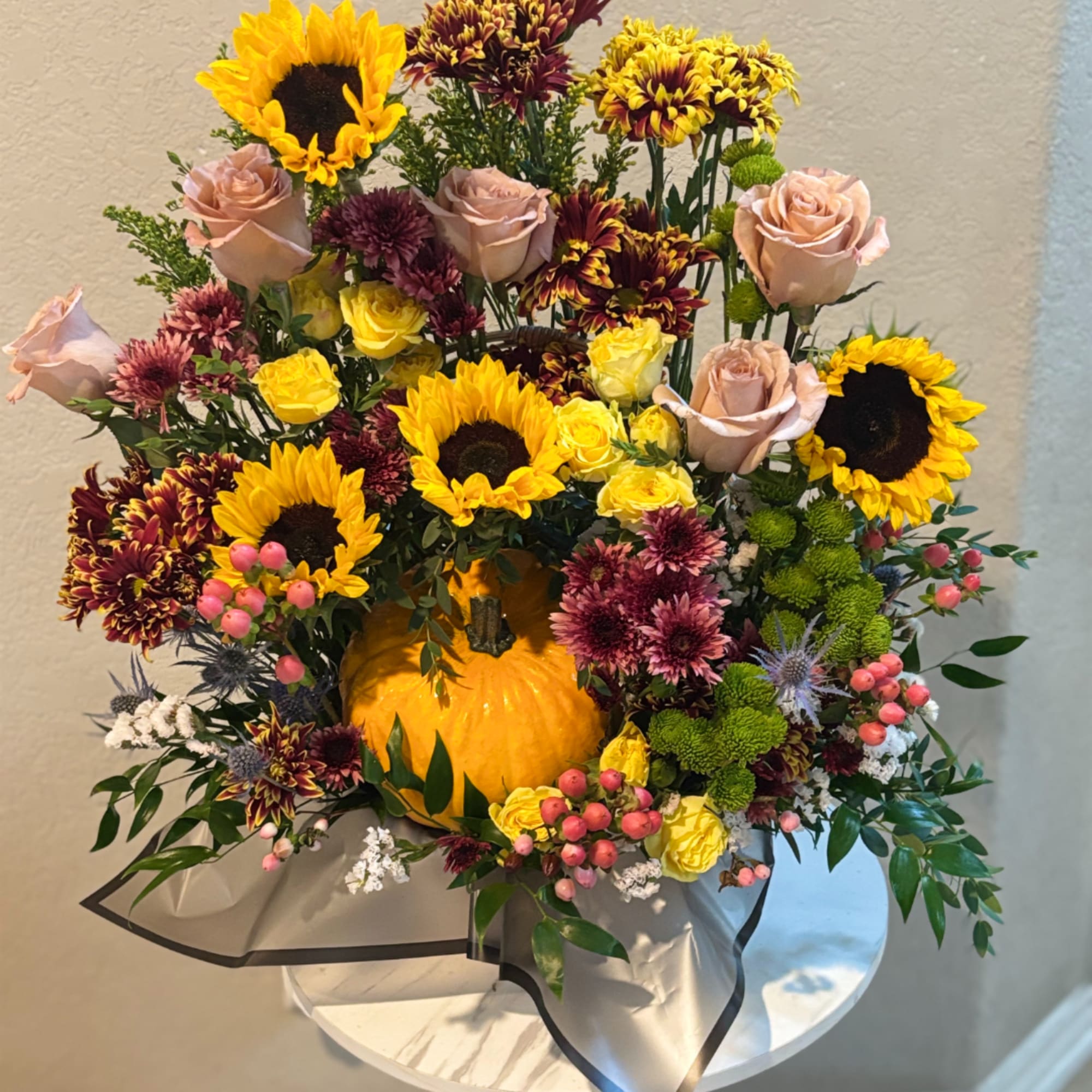 Autumn floral arrangement with sunflowers, roses, and chrysanthemums around a pumpkin