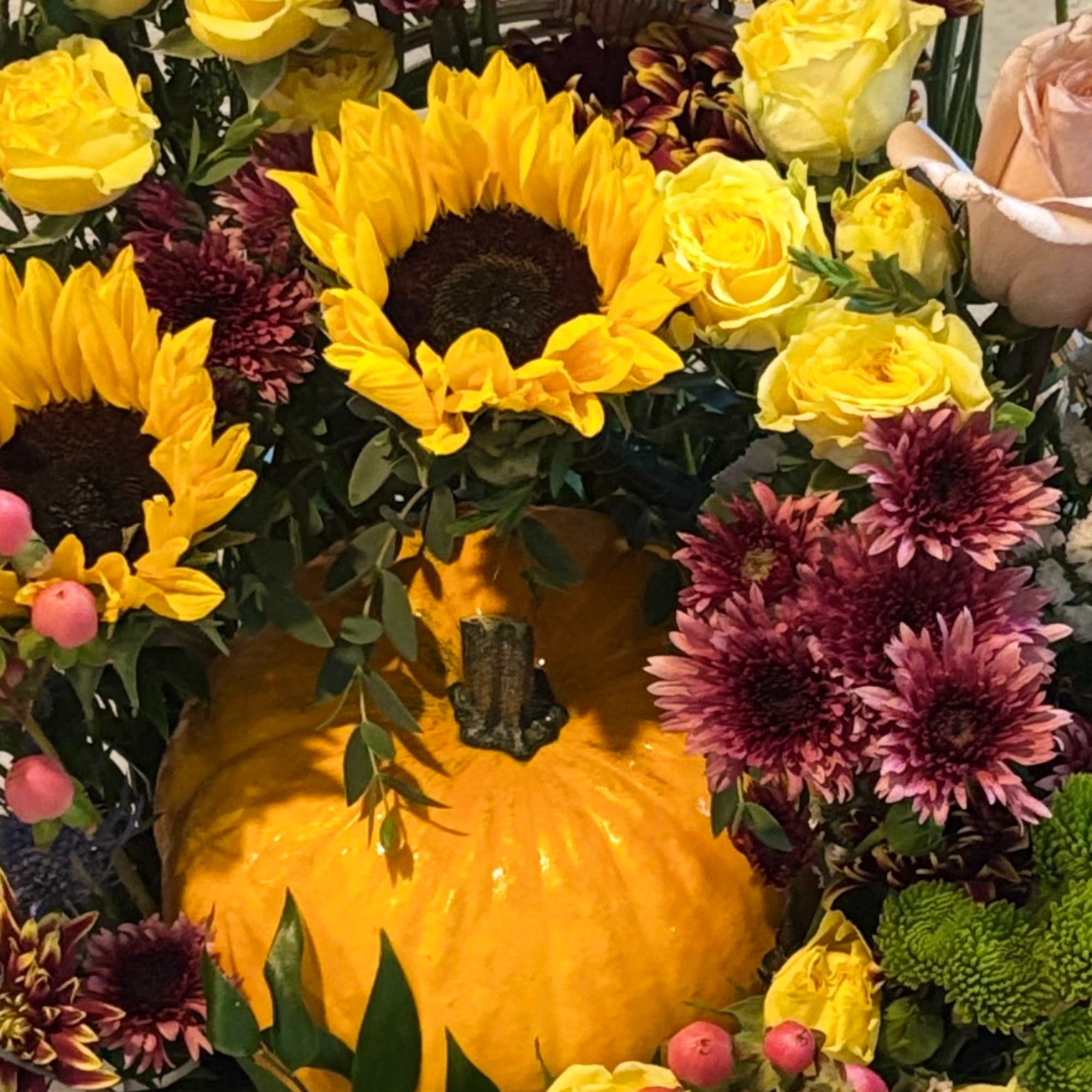 Sunflowers and yellow roses arranged around a pumpkin centerpiece