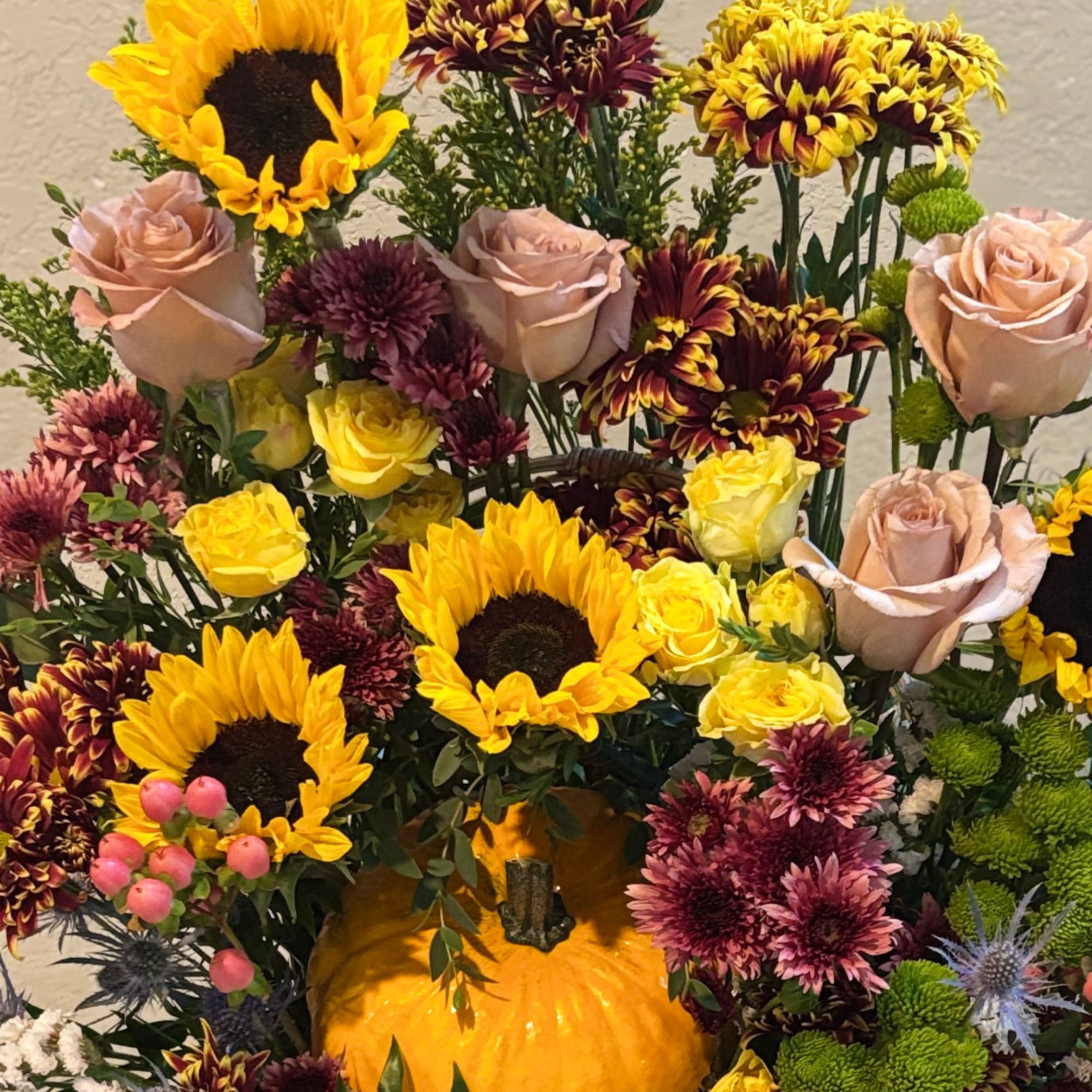Mixed bouquet with sunflowers, roses, and chrysanthemums around a pumpkin