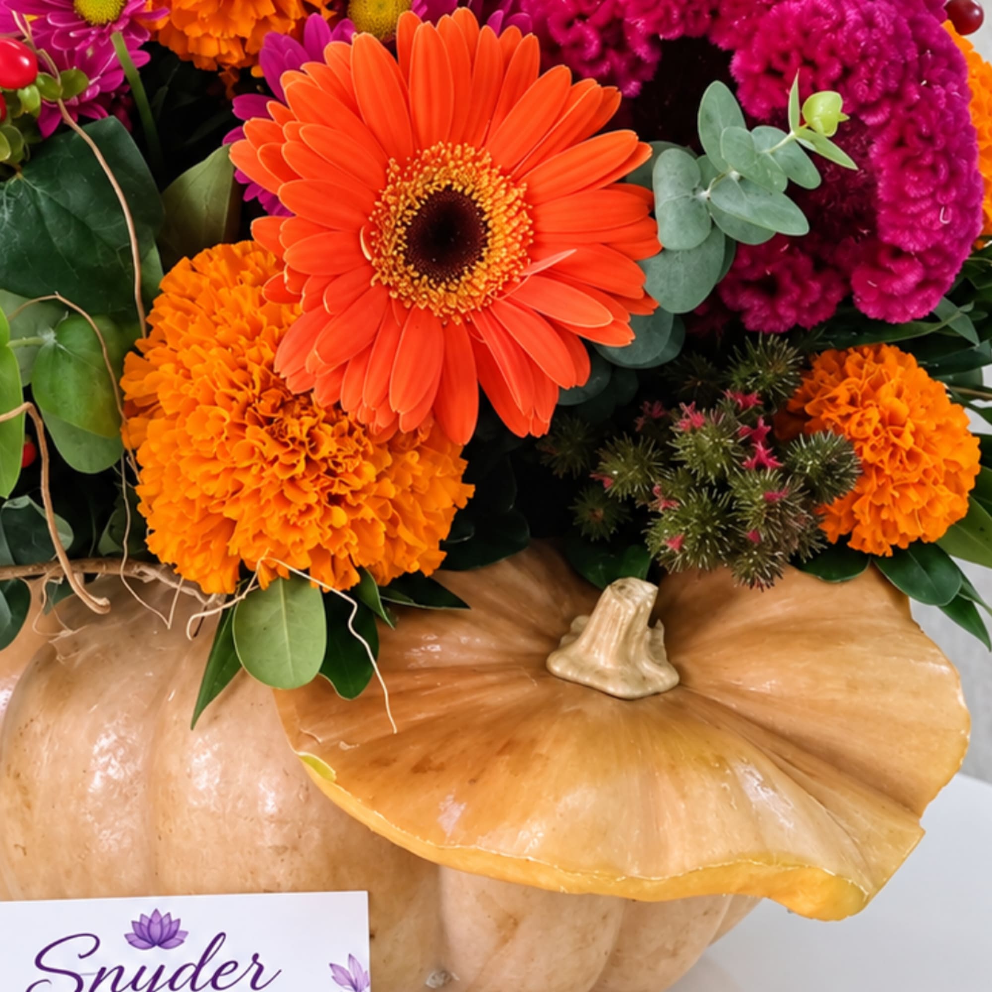 Orange and magenta flowers arranged in a pumpkin container