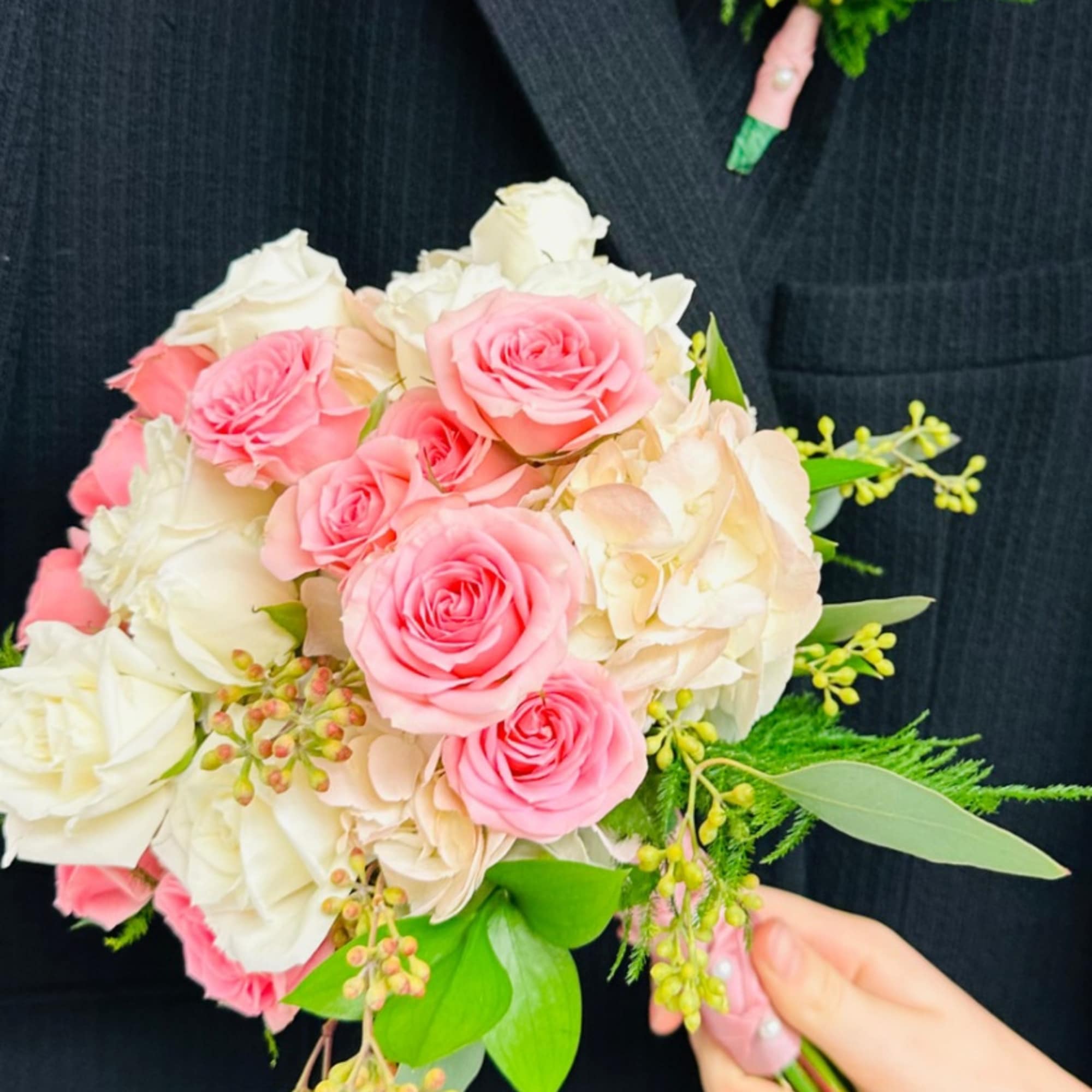 Pink and white rose bouquet with greenery, plus a matching boutonniere on a dark suit