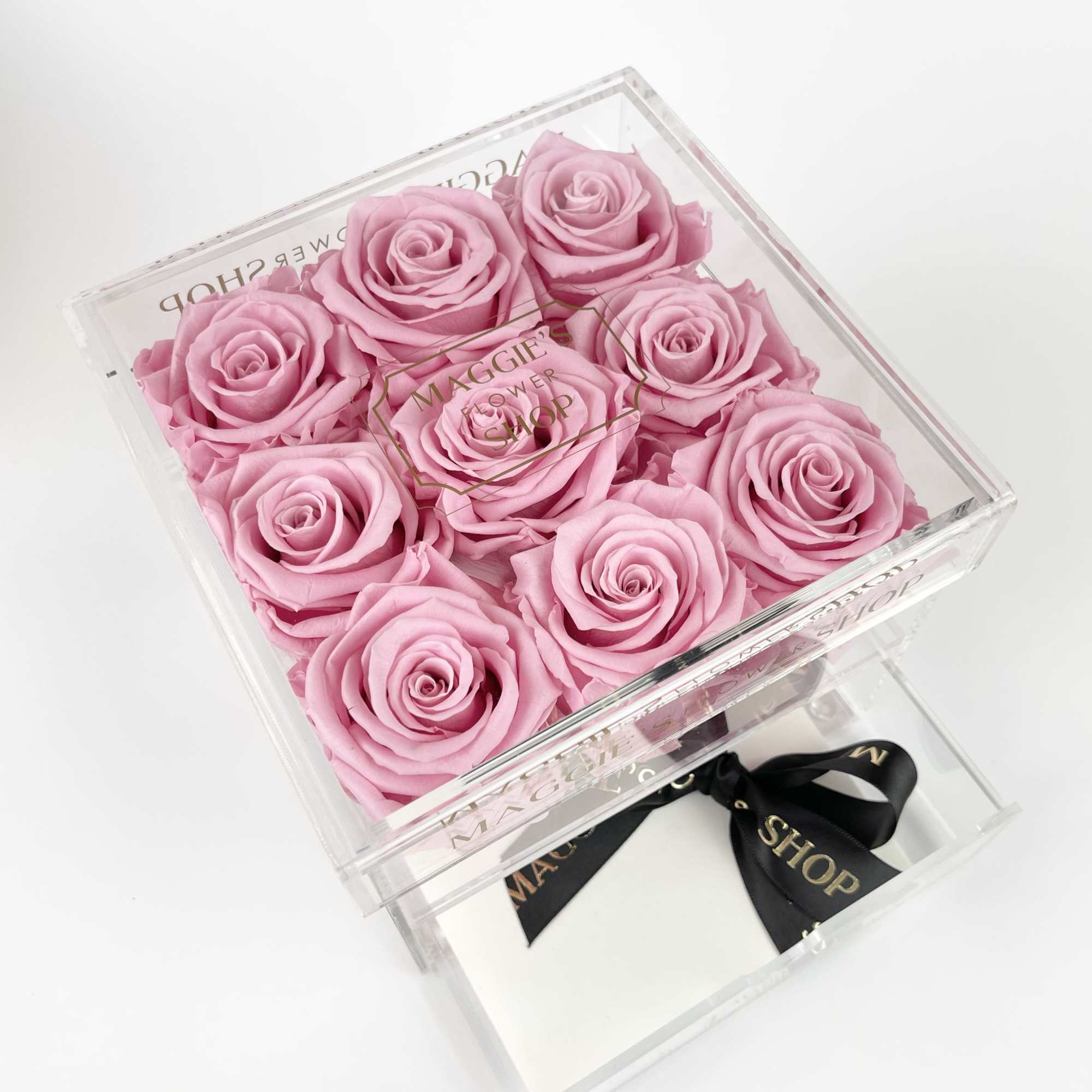 Pink roses arranged in a clear square gift box with a ribbon