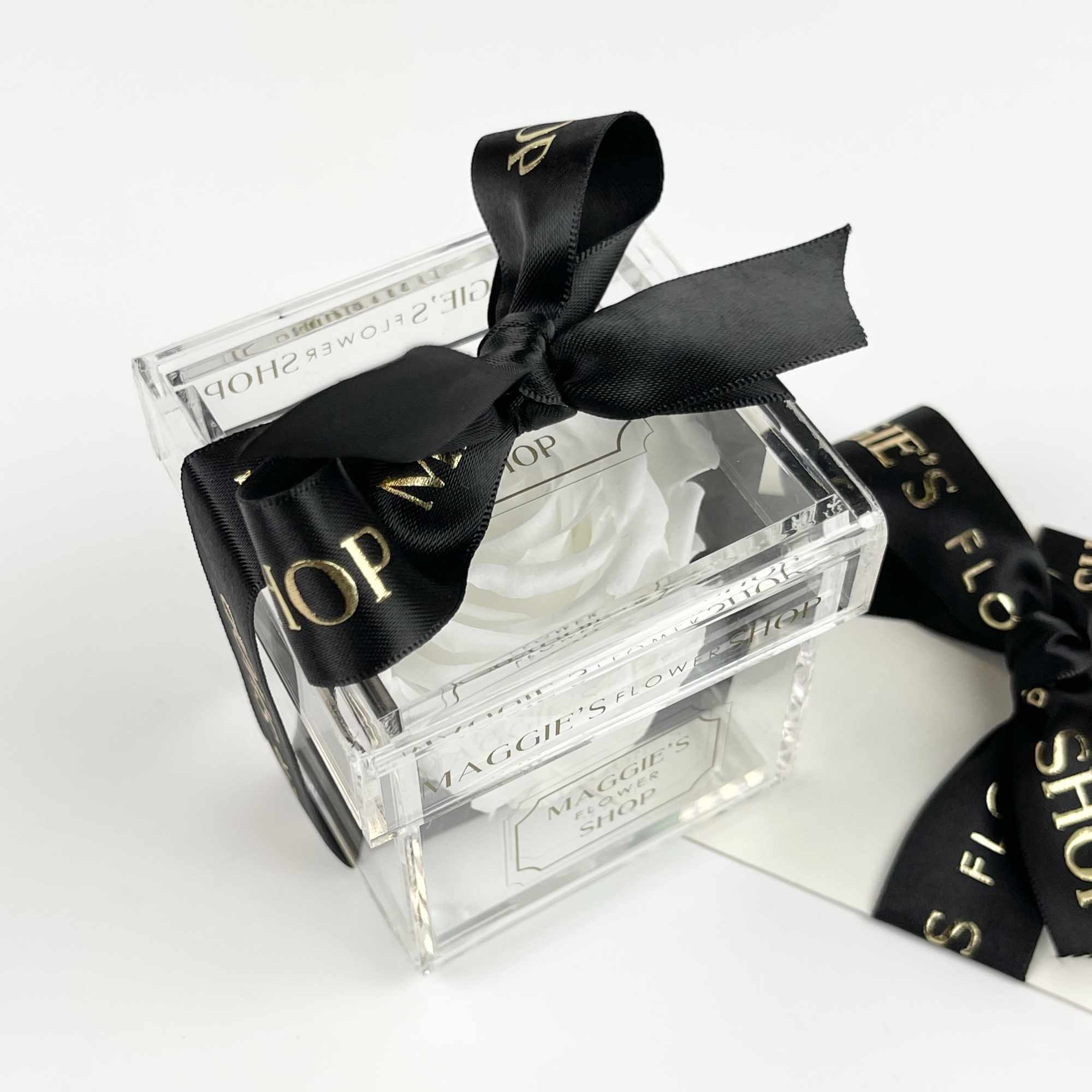 Clear acrylic flower box tied with a black ribbon and white rose inside