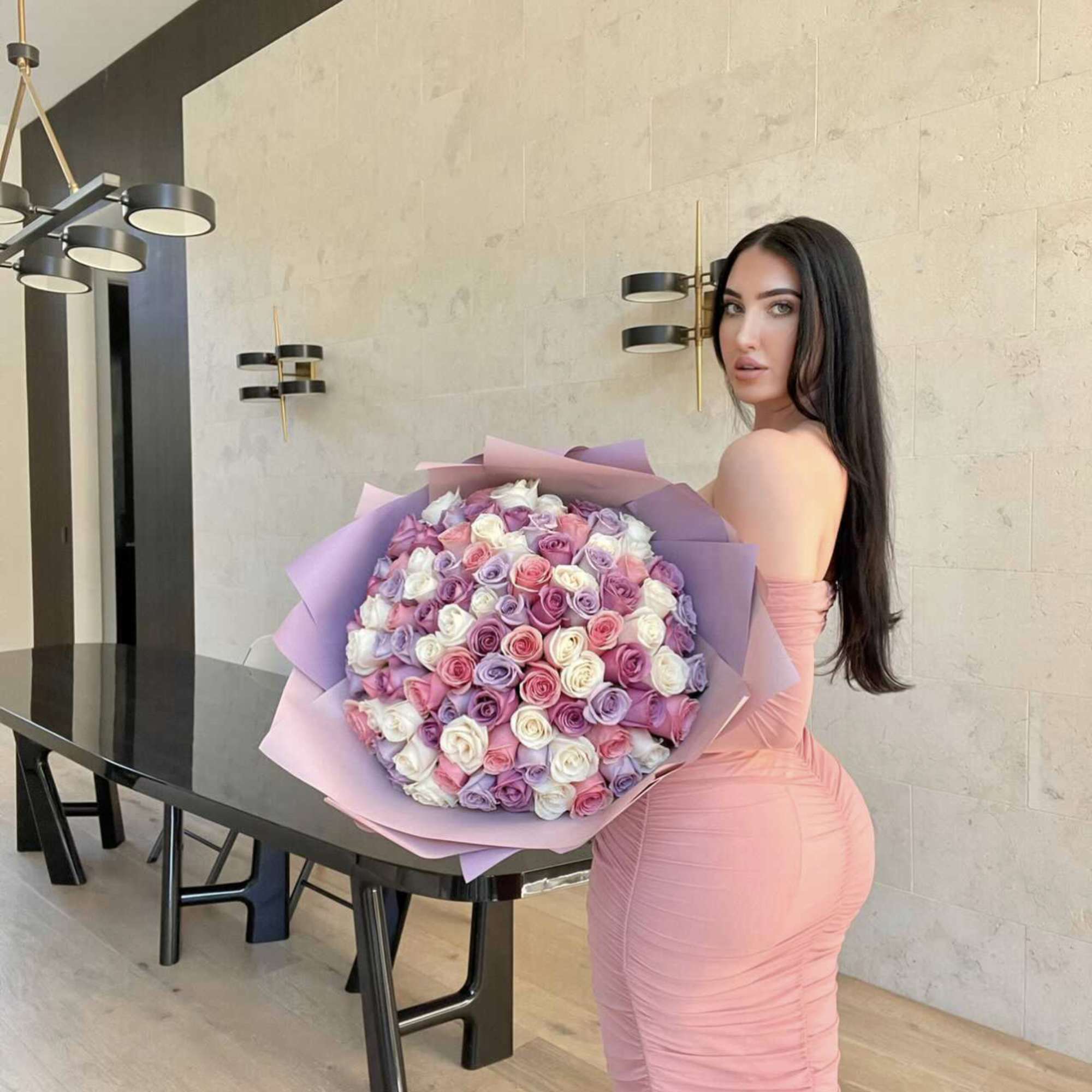 Woman holding a large bouquet of pastel roses wrapped in lavender paper