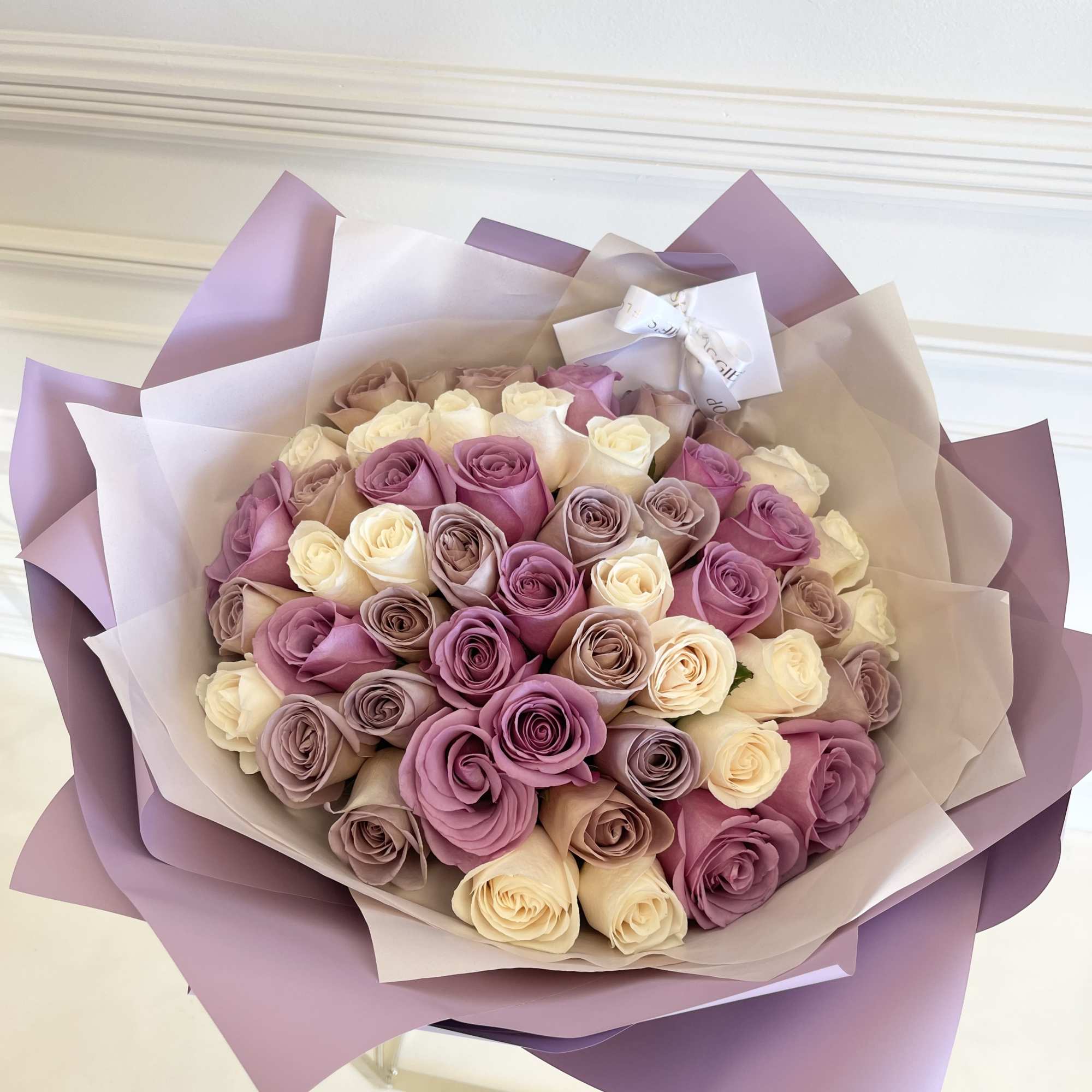 Bouquet of pink, lavender, and cream roses wrapped in purple paper