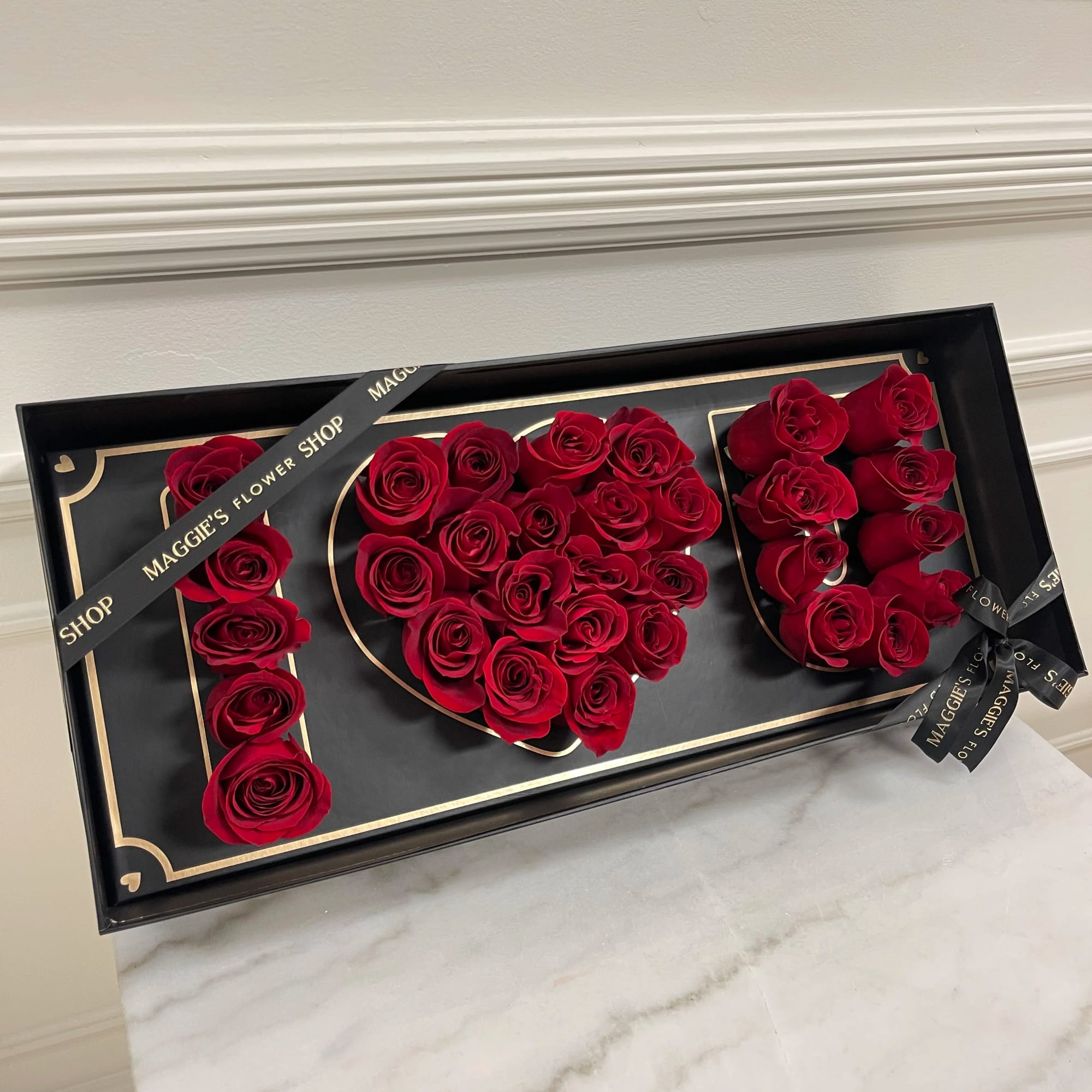 Red roses arranged in a black gift box to form the word LOVE
