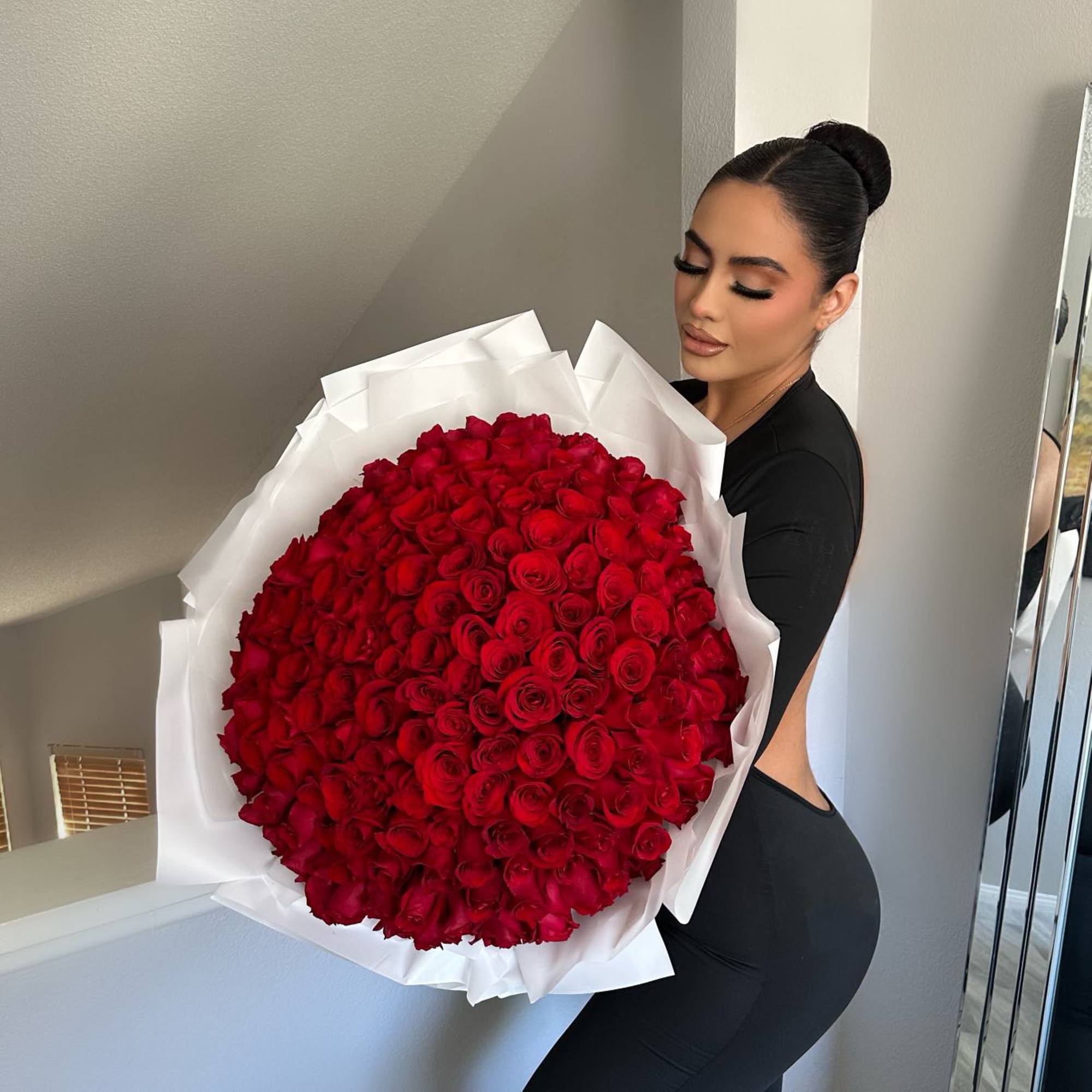 Woman holding a large bouquet of red roses wrapped in white paper