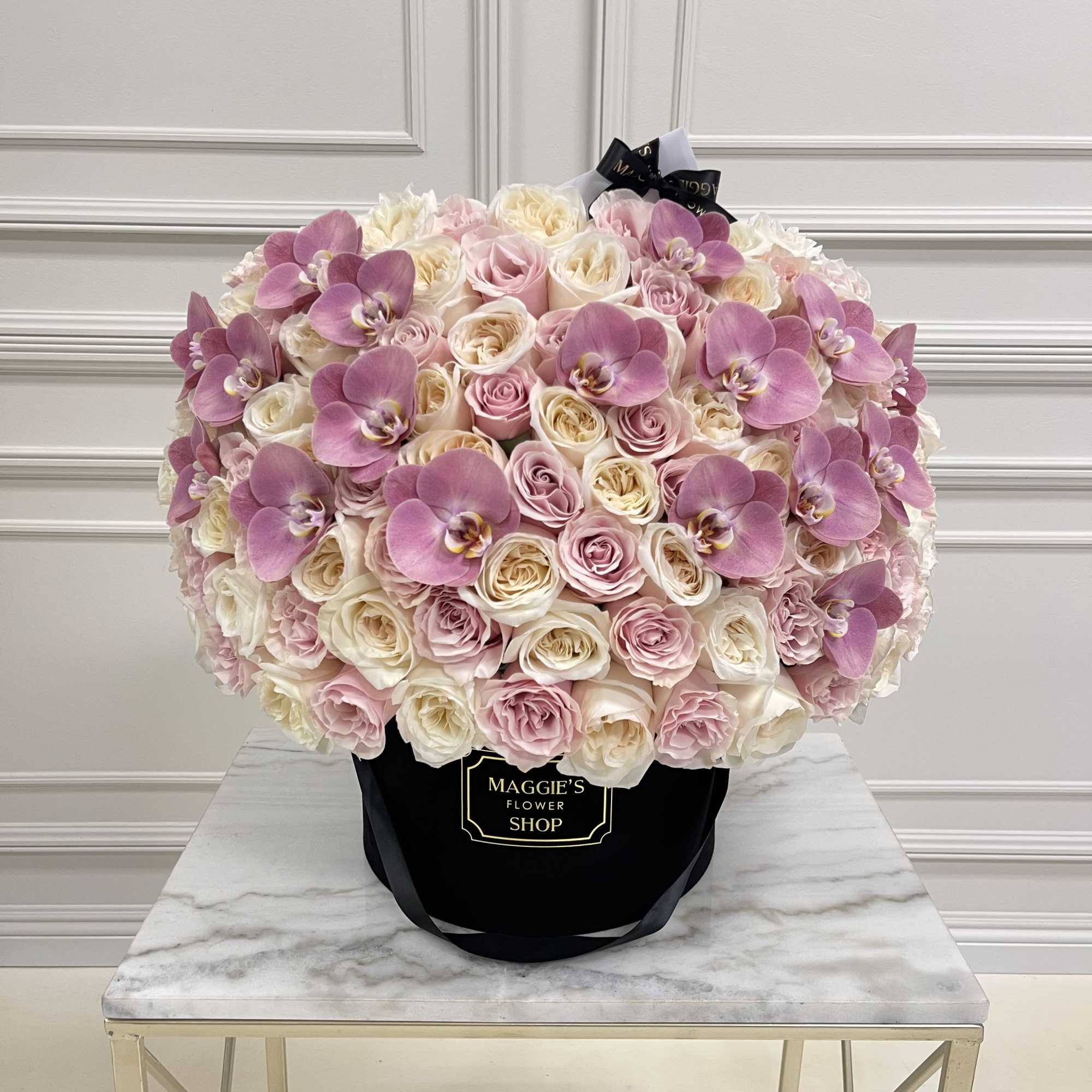 Large bouquet of pink and white roses with purple orchids in a black hat box