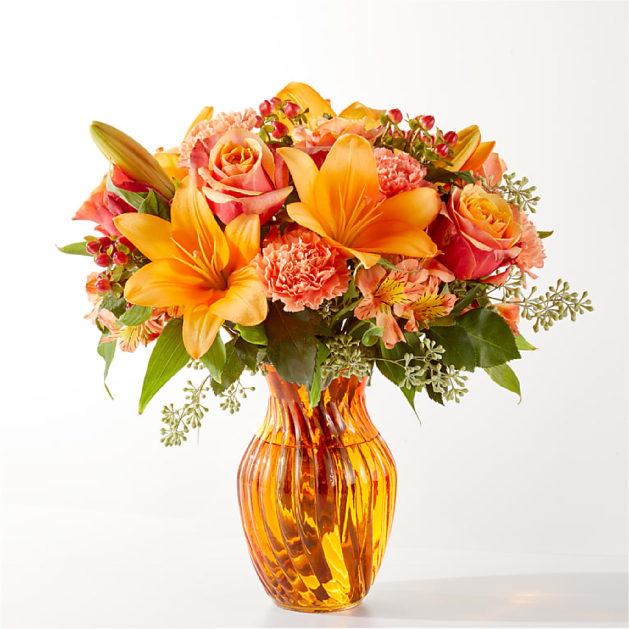 Orange lilies and roses arranged in an amber glass vase