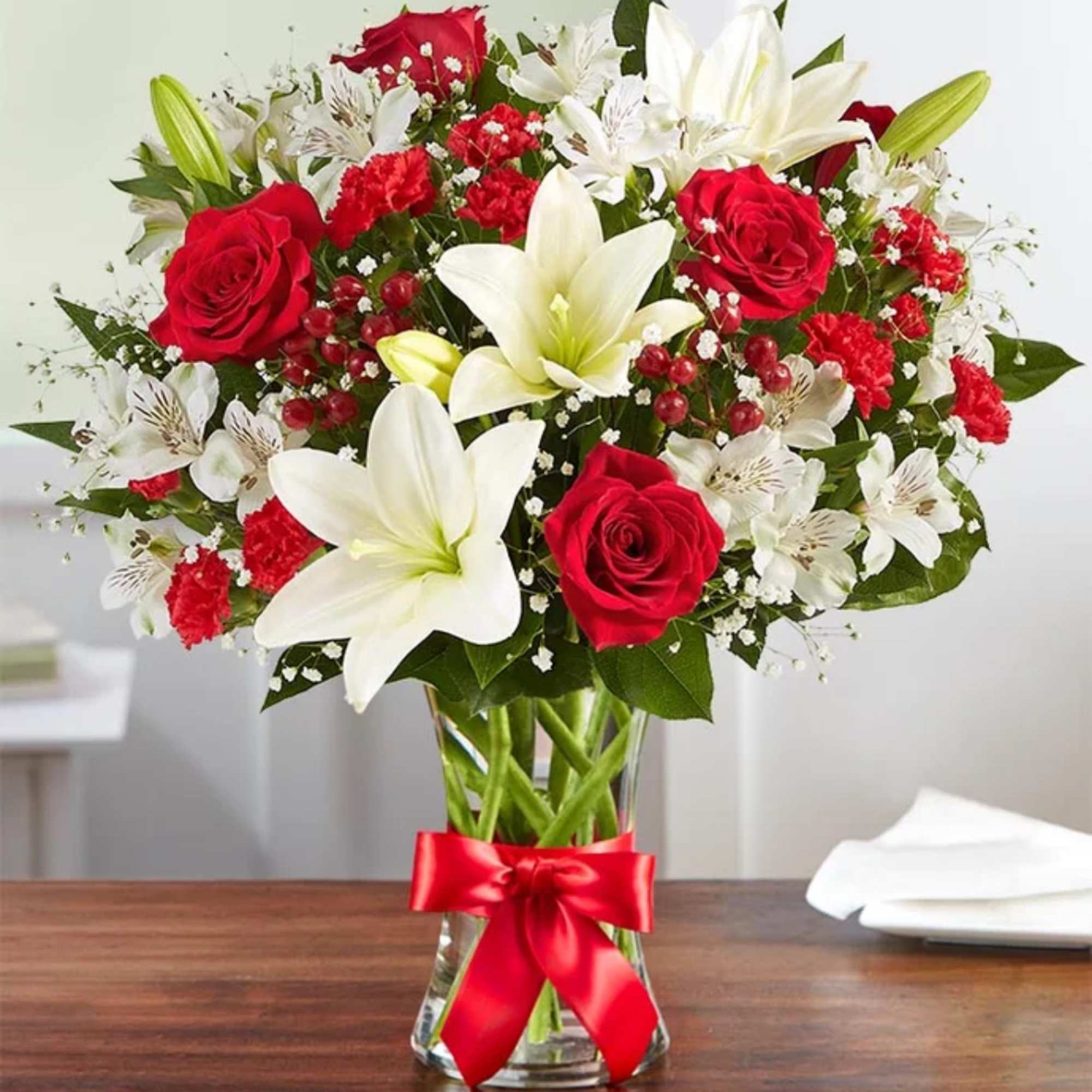 Red roses, white lilies, and mixed red and white flowers in a clear vase with a red bow