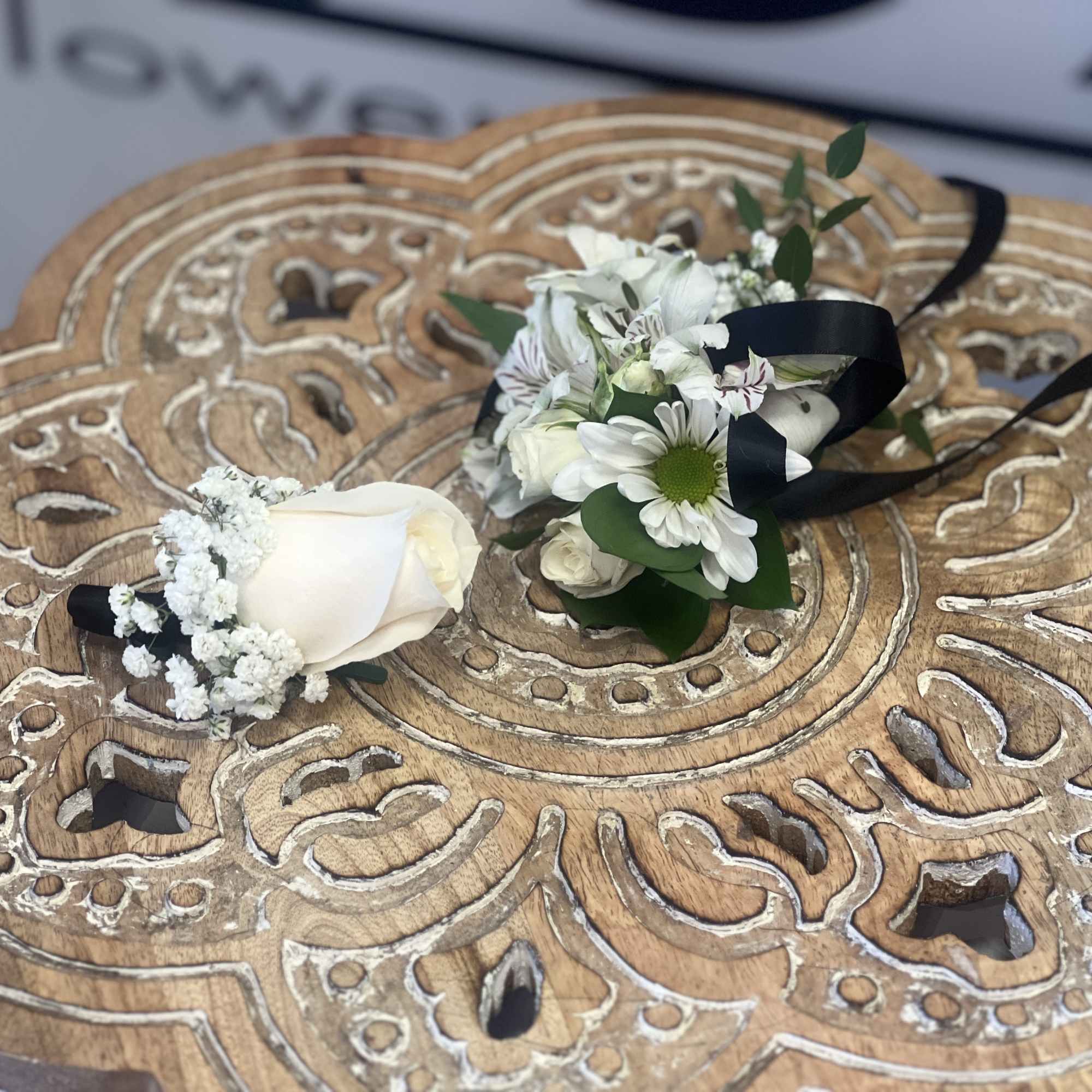 White rose boutonniere and white daisy corsage with black ribbon on a carved wooden tray