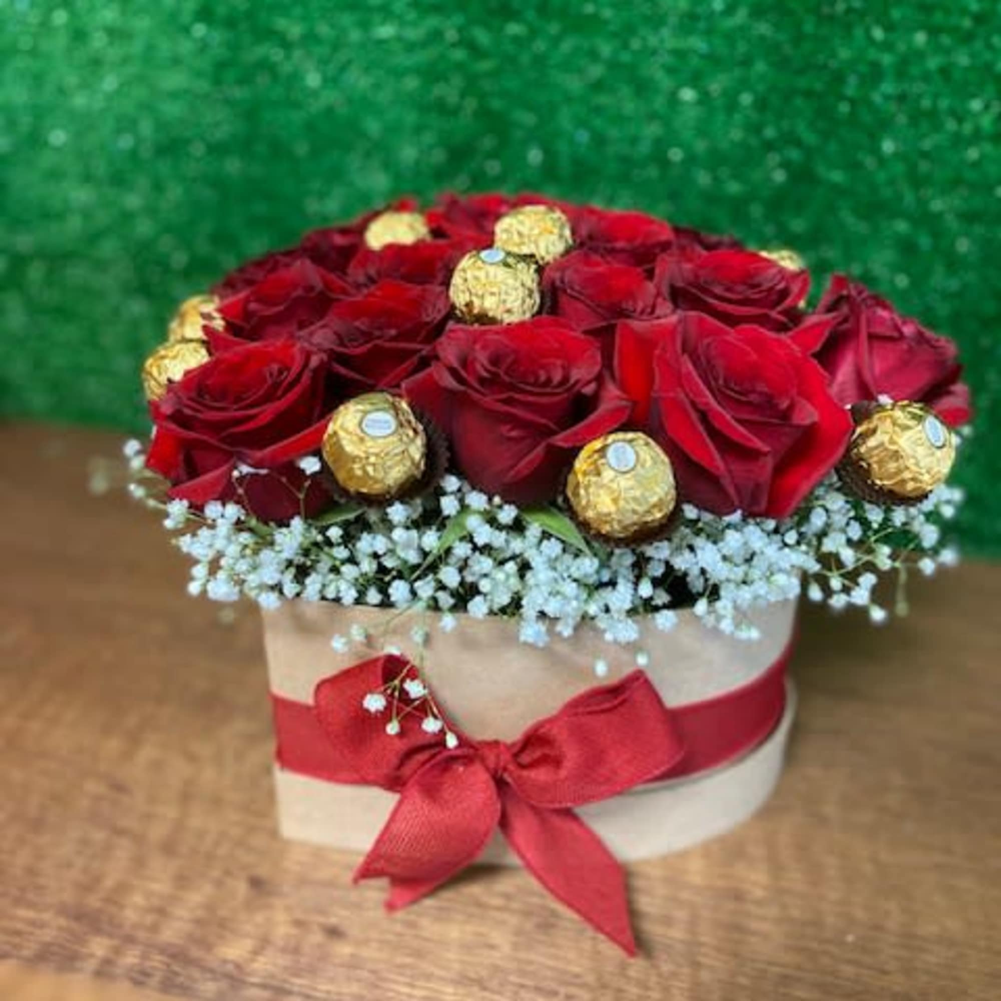 Round box of red roses and gold-wrapped chocolates with white filler flowers.