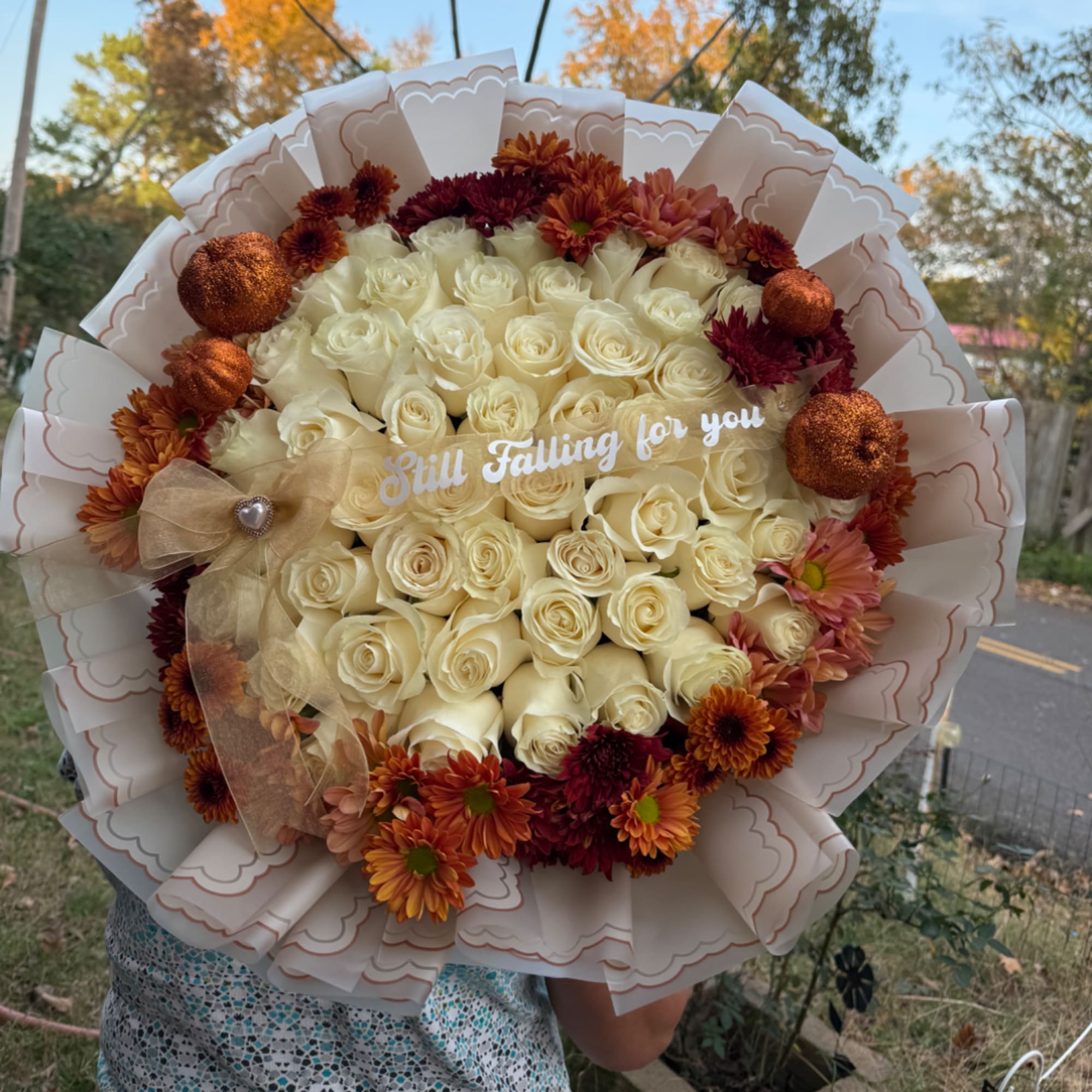 Cream rose bouquet with orange and burgundy flowers and a "Still Falling for you" sign